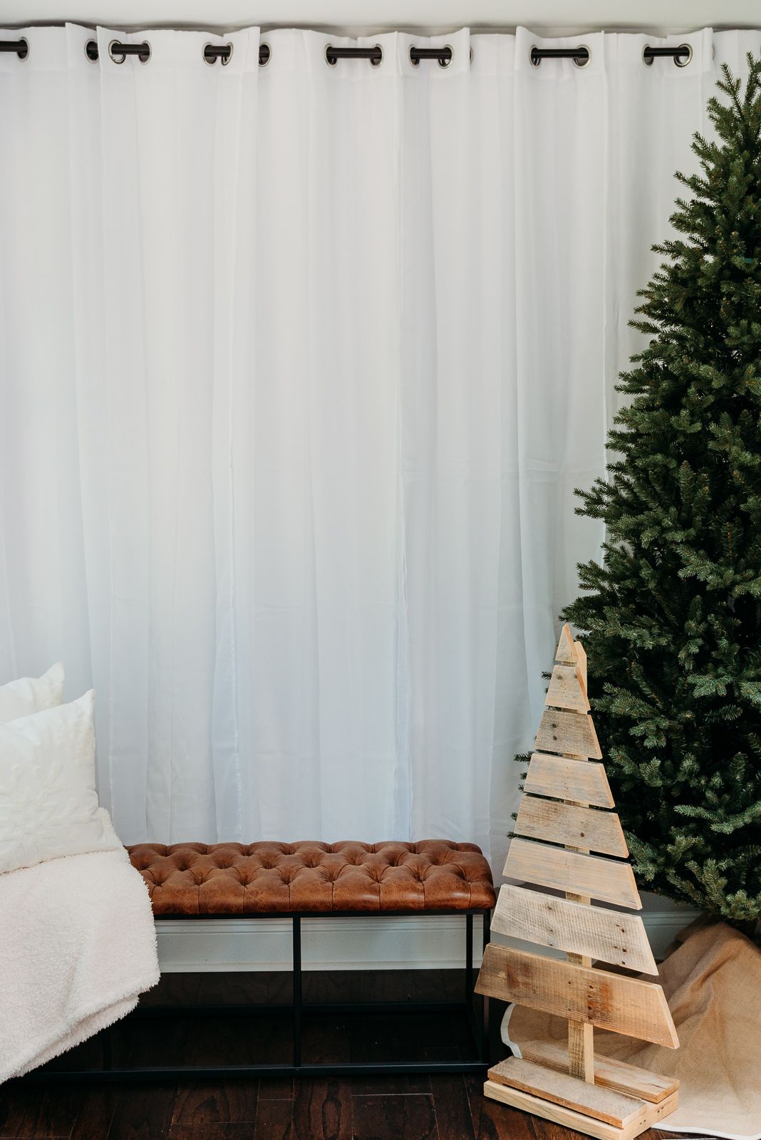 Modern holiday decor featuring wooden triangle tree, brown leather bench and artificial Christmas tree.