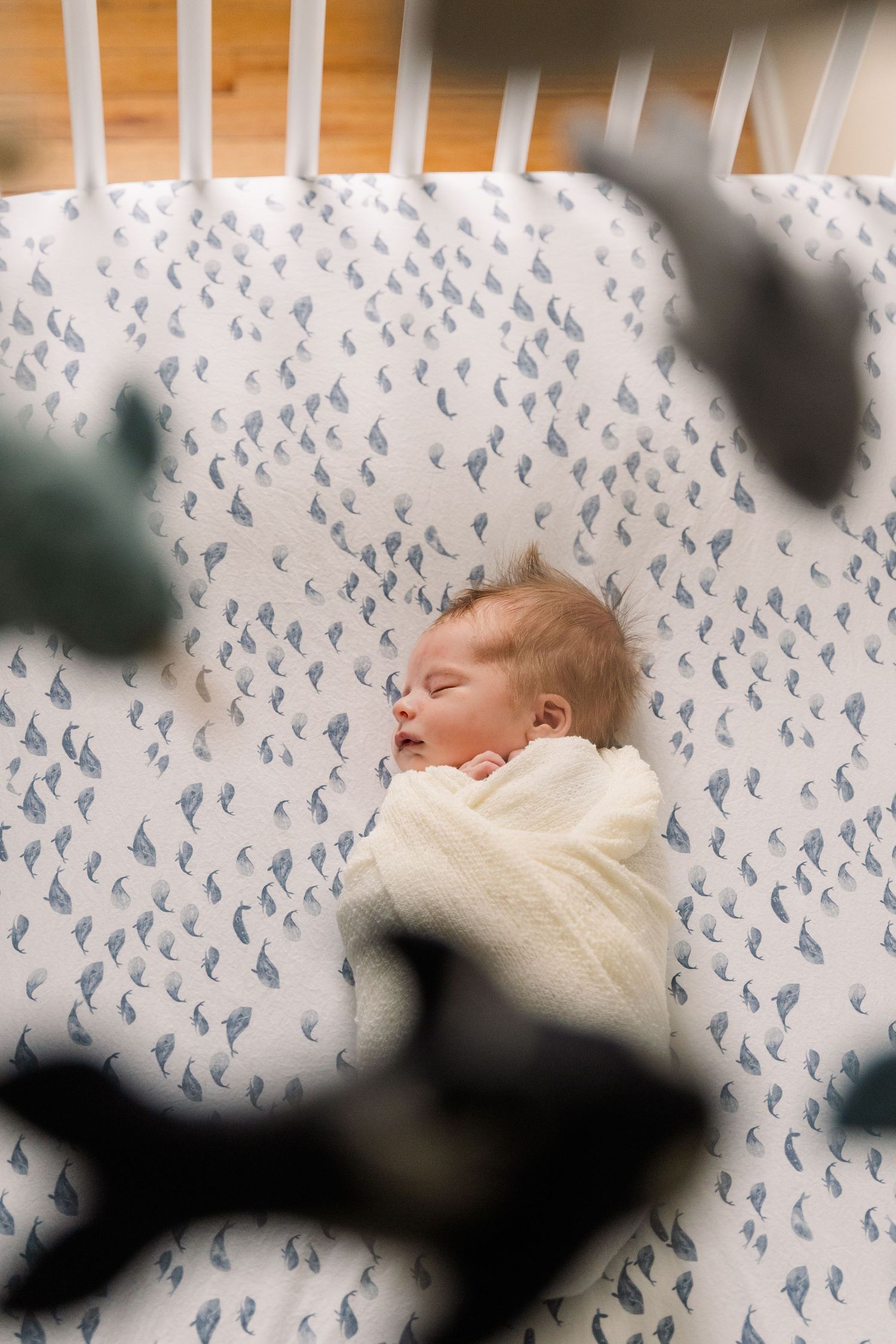 Sleeping baby on patterned sheet with blue birds, viewed through crib slats.