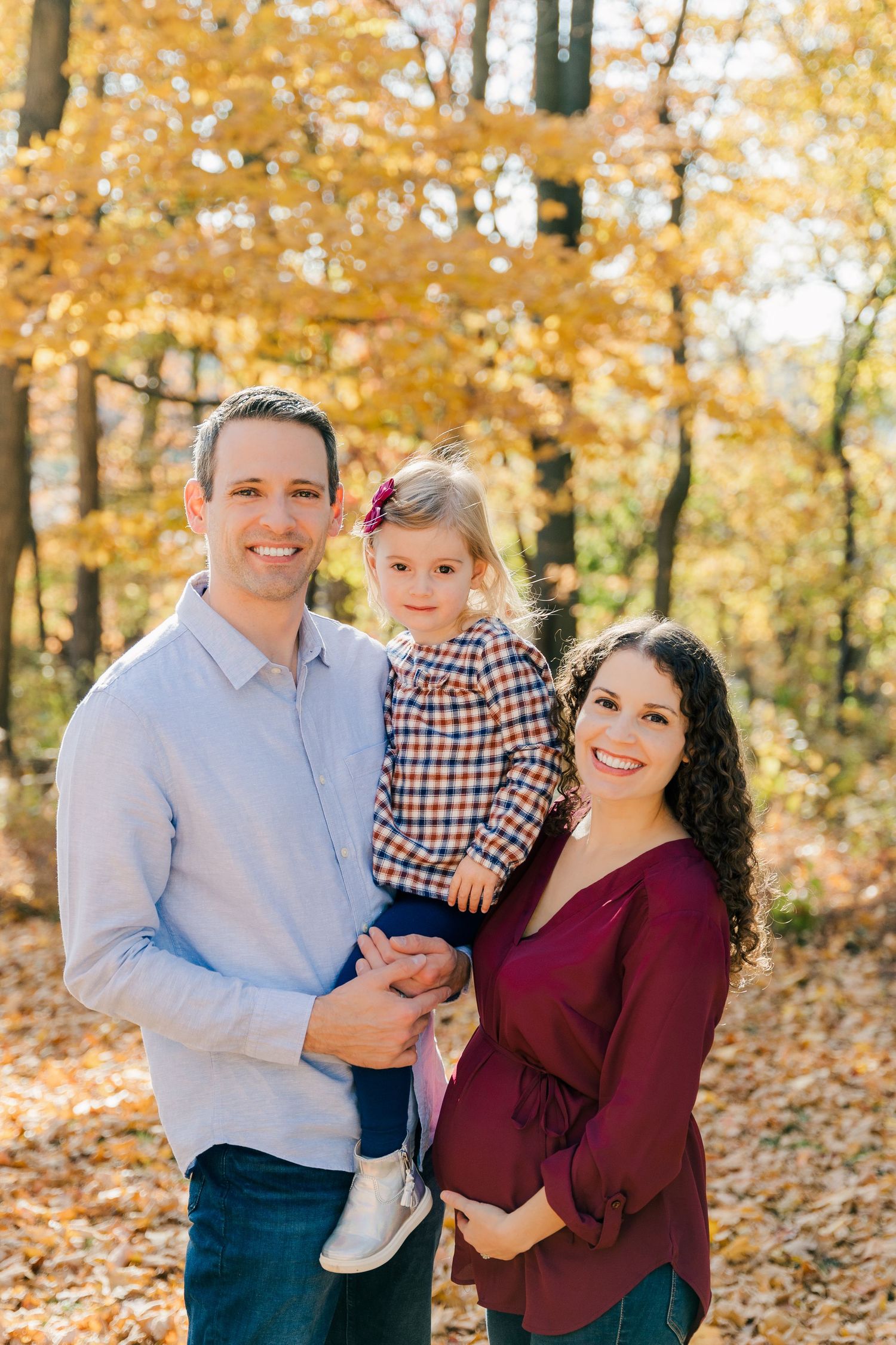 Family portrait in autumn forest with golden leaves and sunlight.