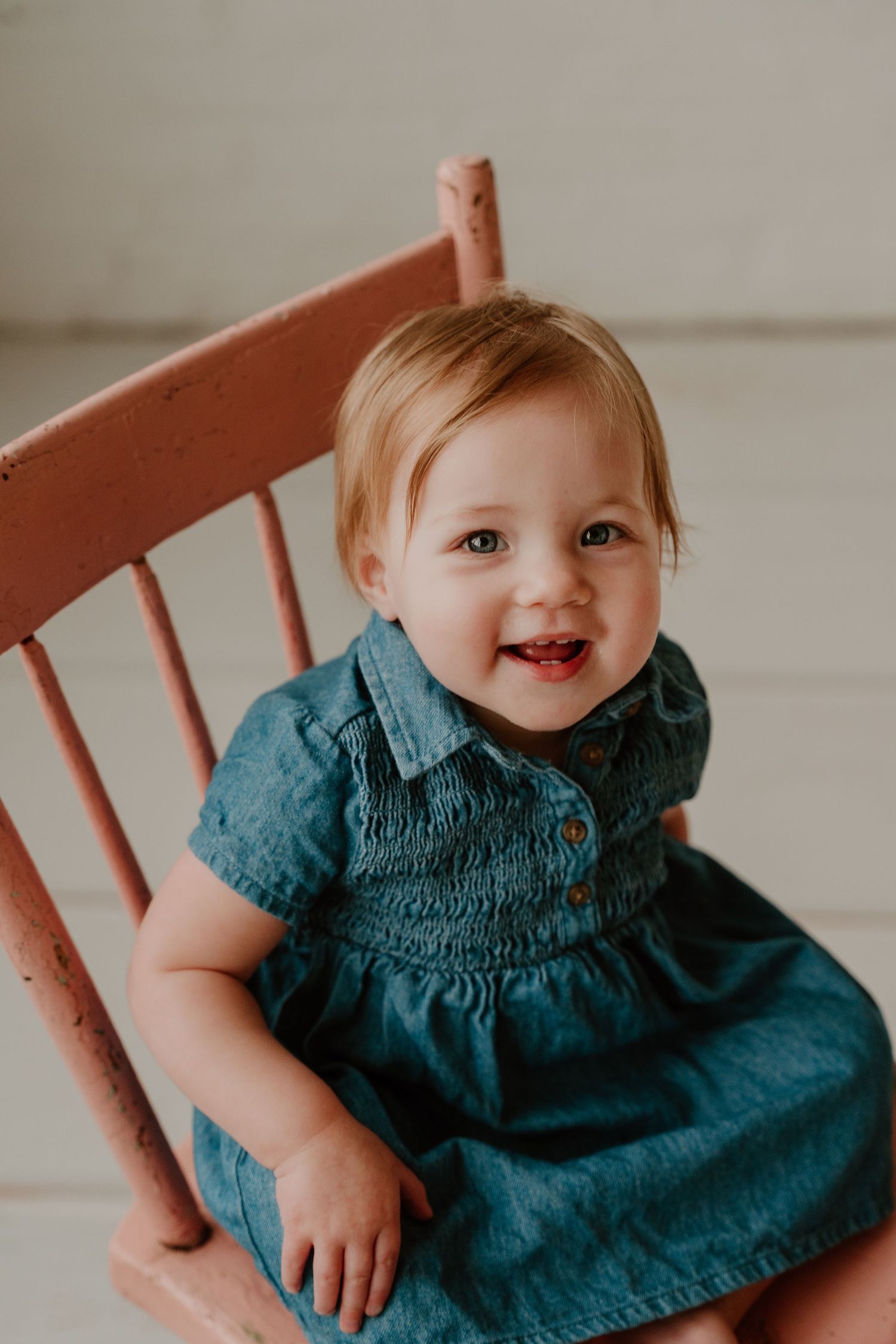 A series of five photos showing a small child in a navy blue dress sitting and smiling in a pink wooden chair.