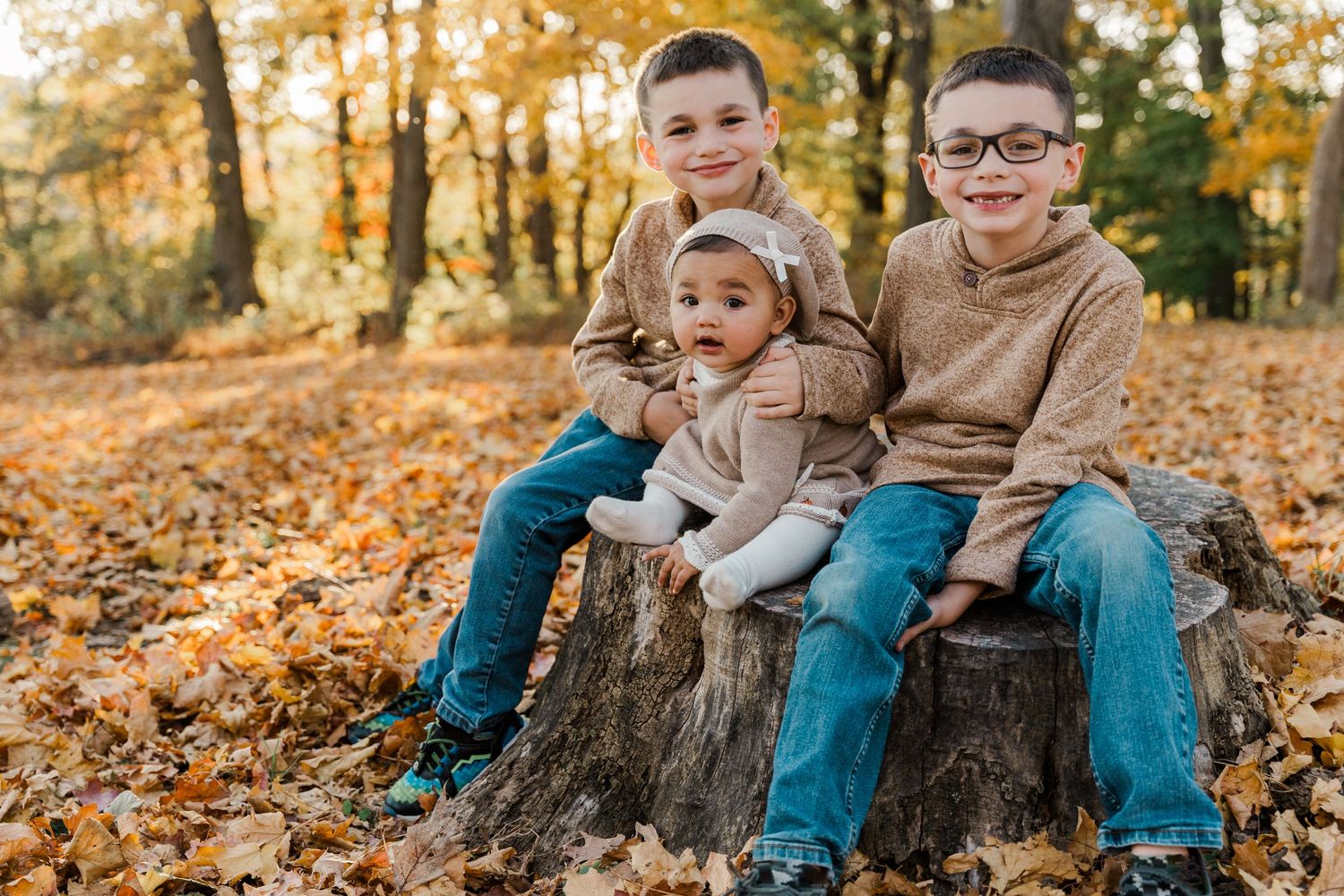 Three siblings sitting together on tree stump in autumn forest.