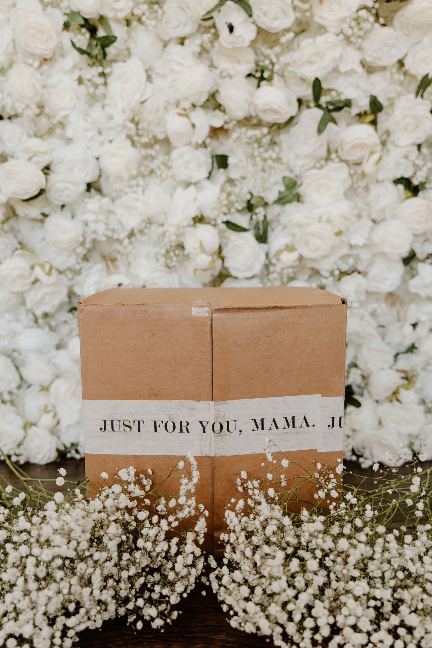 A brown cardboard box surrounded by delicate white flowers and baby's breath with text reading 'Just for you, mama'.