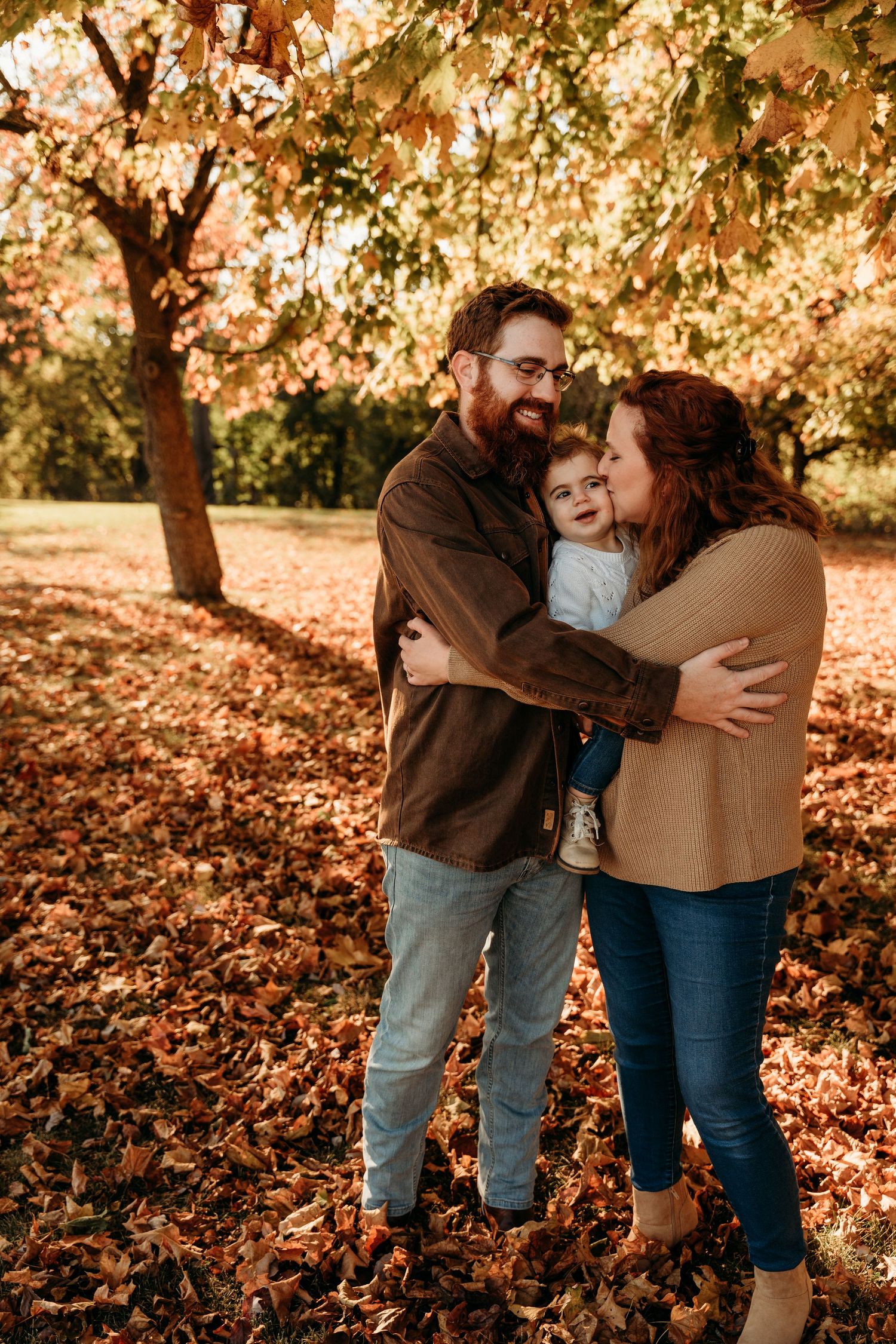 Family embracing in warm autumn setting with fallen leaves.