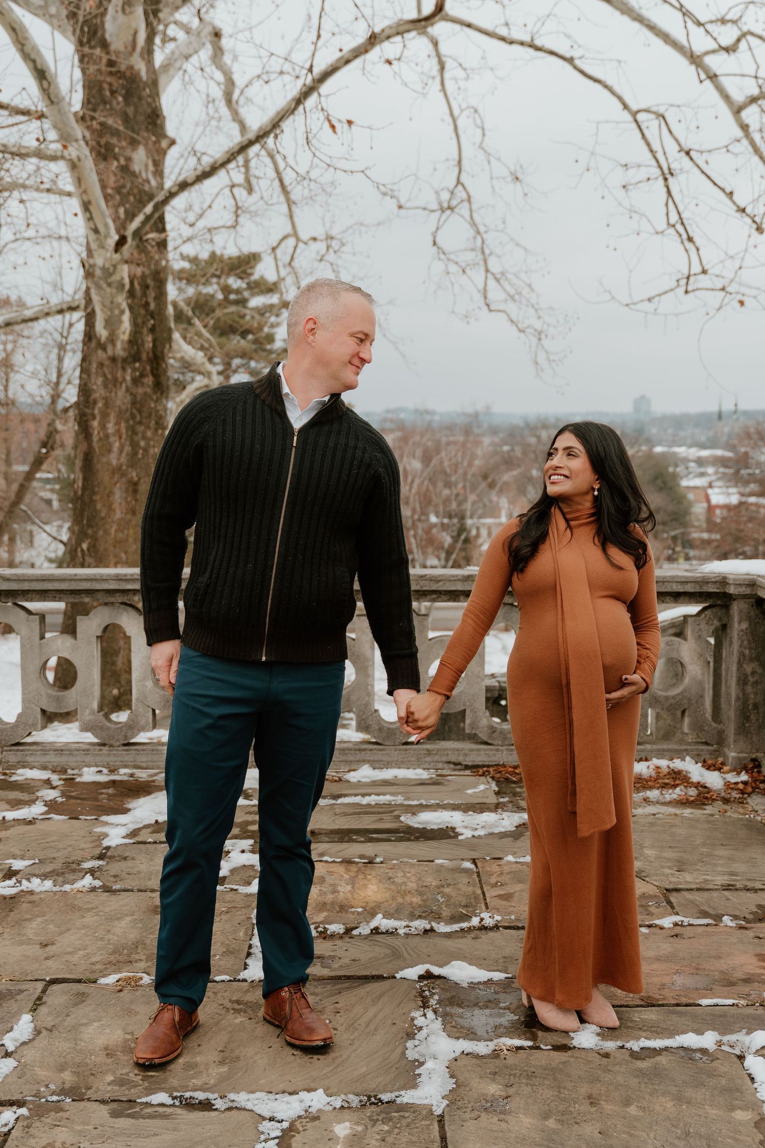 A couple in winter attire shares a tender moment while standing in the snow at a scenic overlook.