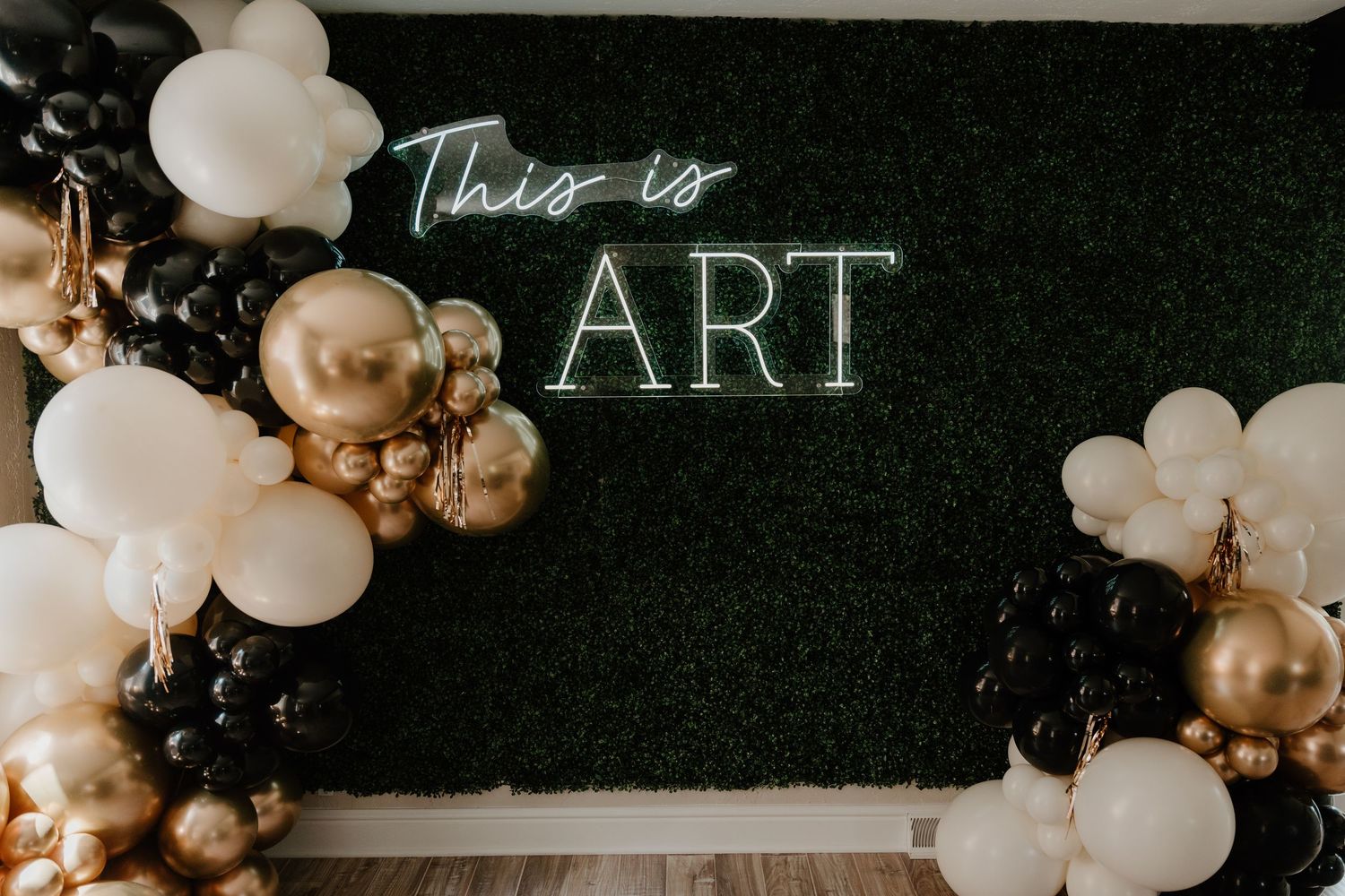 Wedding reception venue decorated with elegant white and gold balloon arrangements and neon signage on dark walls.