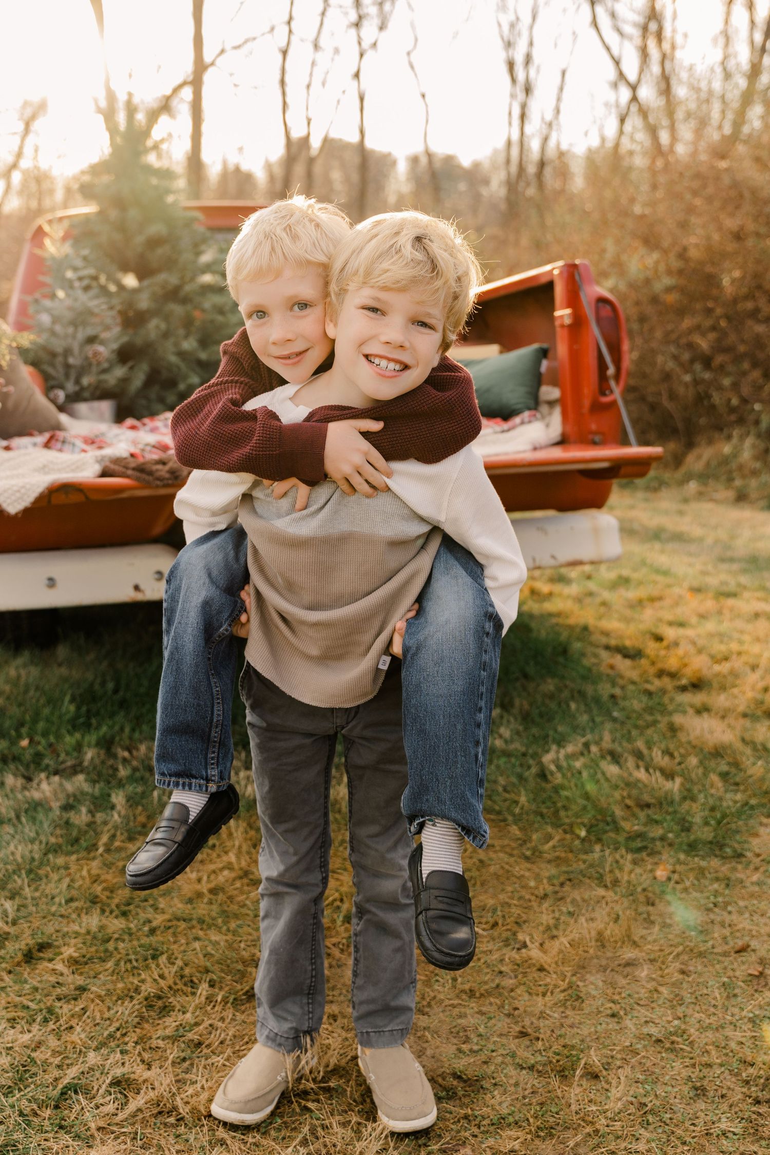 Two children in casual wear playing piggyback ride outdoors at sunset.
