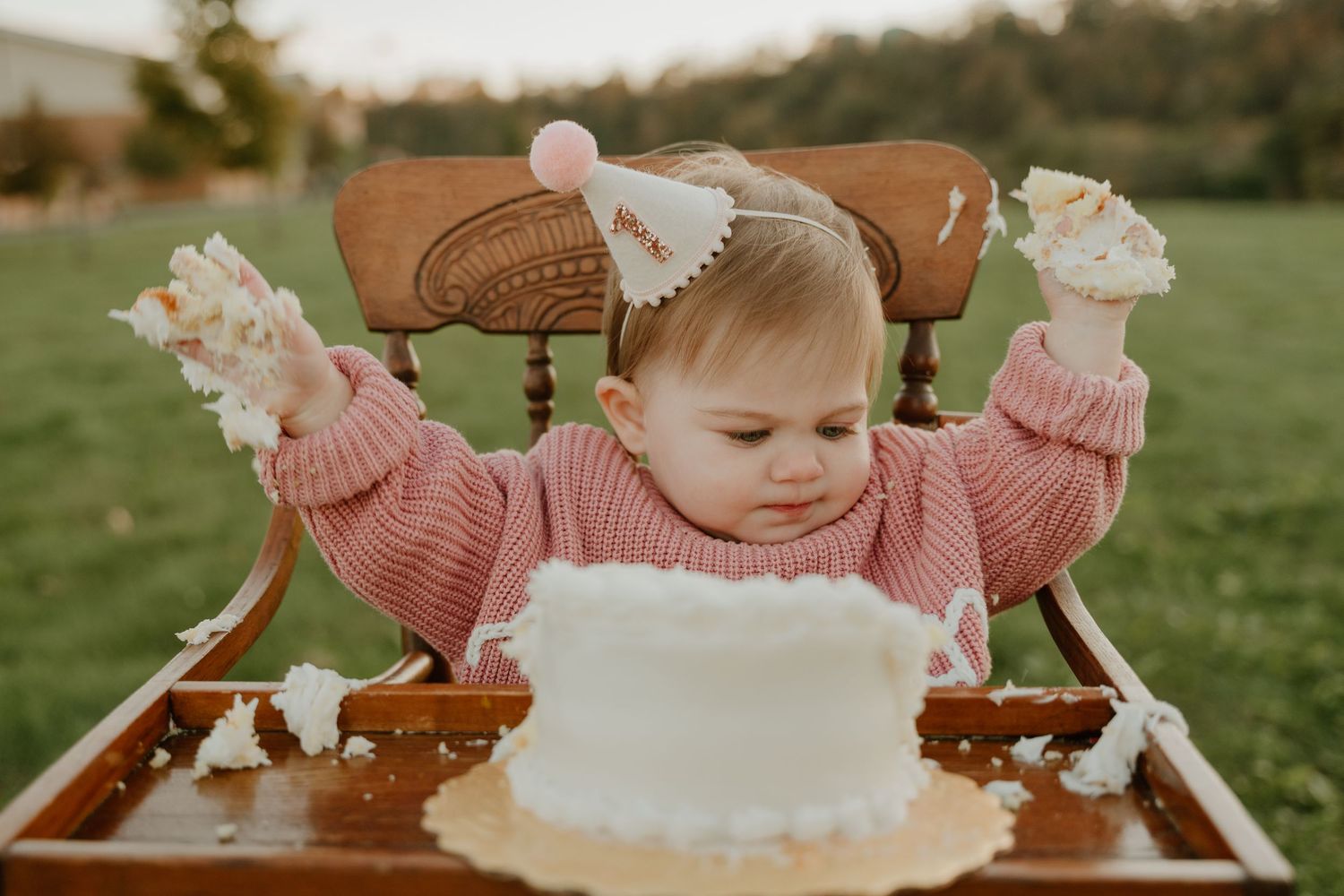 A first birthday celebration in a garden with a white cake and pink decorative details.