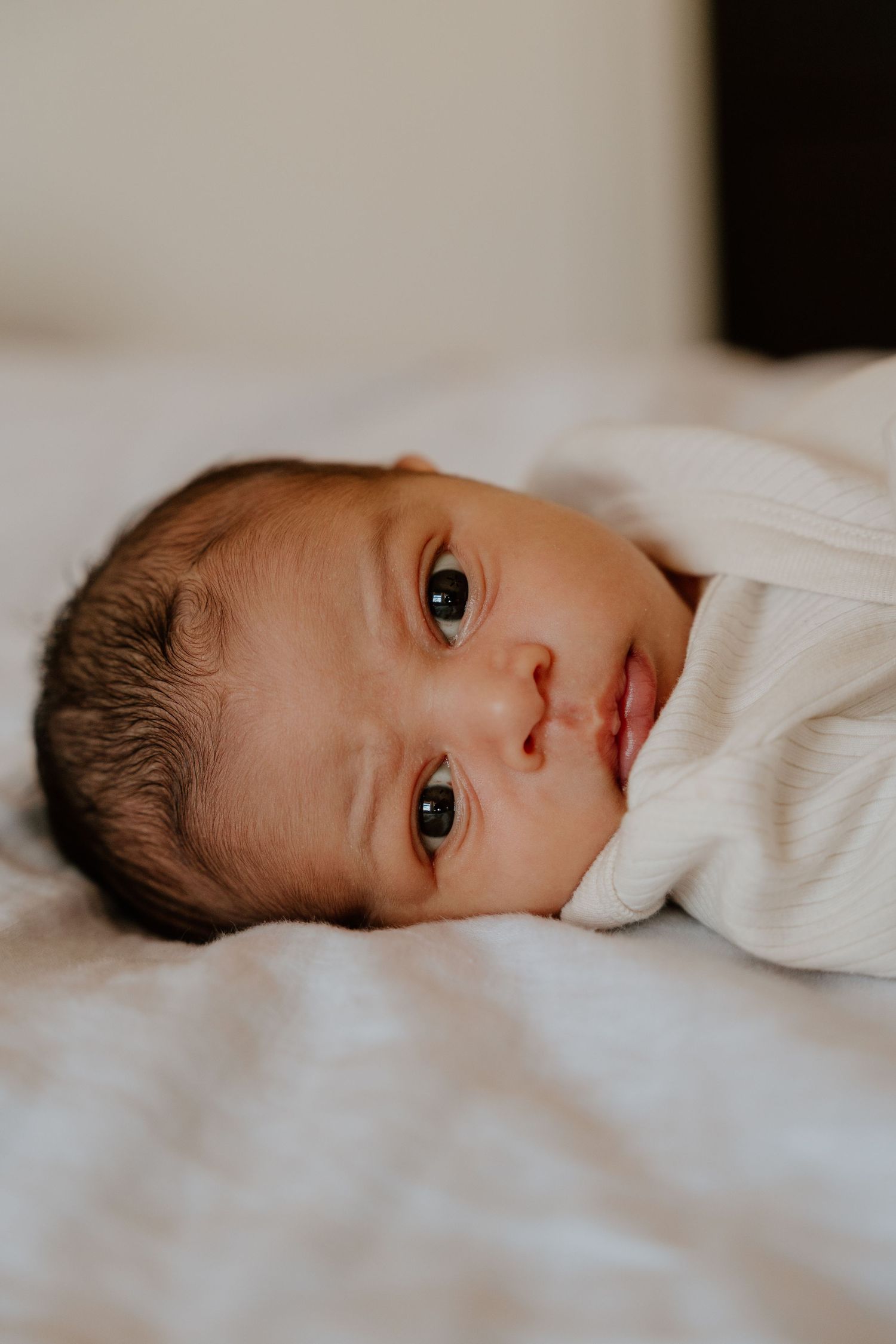 A newborn baby lies on white bedding in a series of side profile views.