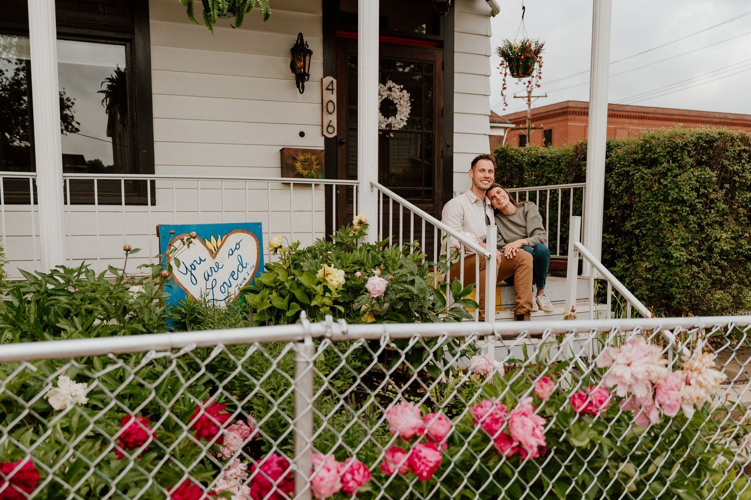 Pink roses bloom along a white lattice fence in front of a house with a porch and white siding.