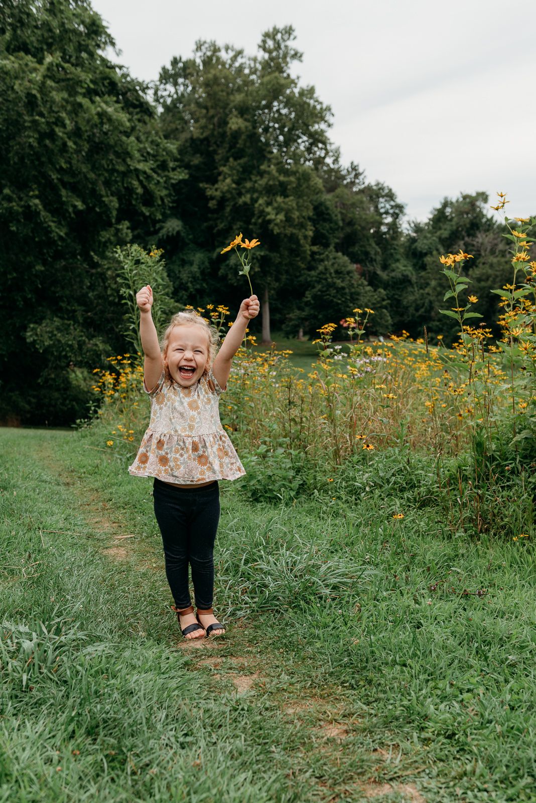 Child in floral dress running joyfully through field of yellow wildflowers.