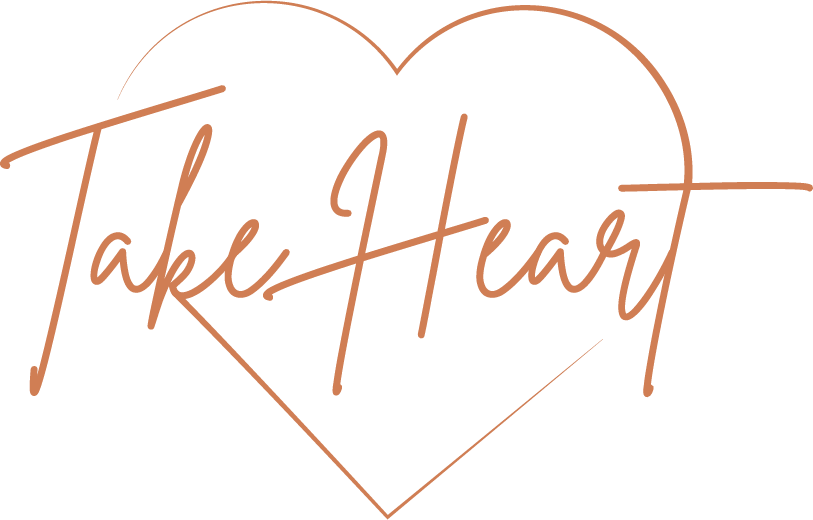 Neon pink light sign saying 'Take Heart' with heart outline against black background.