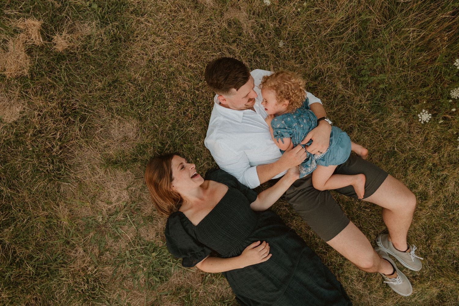 A playful family moment captured from above as they lay in the grass together.