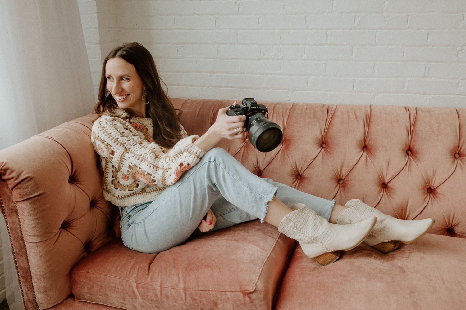 A person in white lounges on a pink tufted couch against a white brick wall.