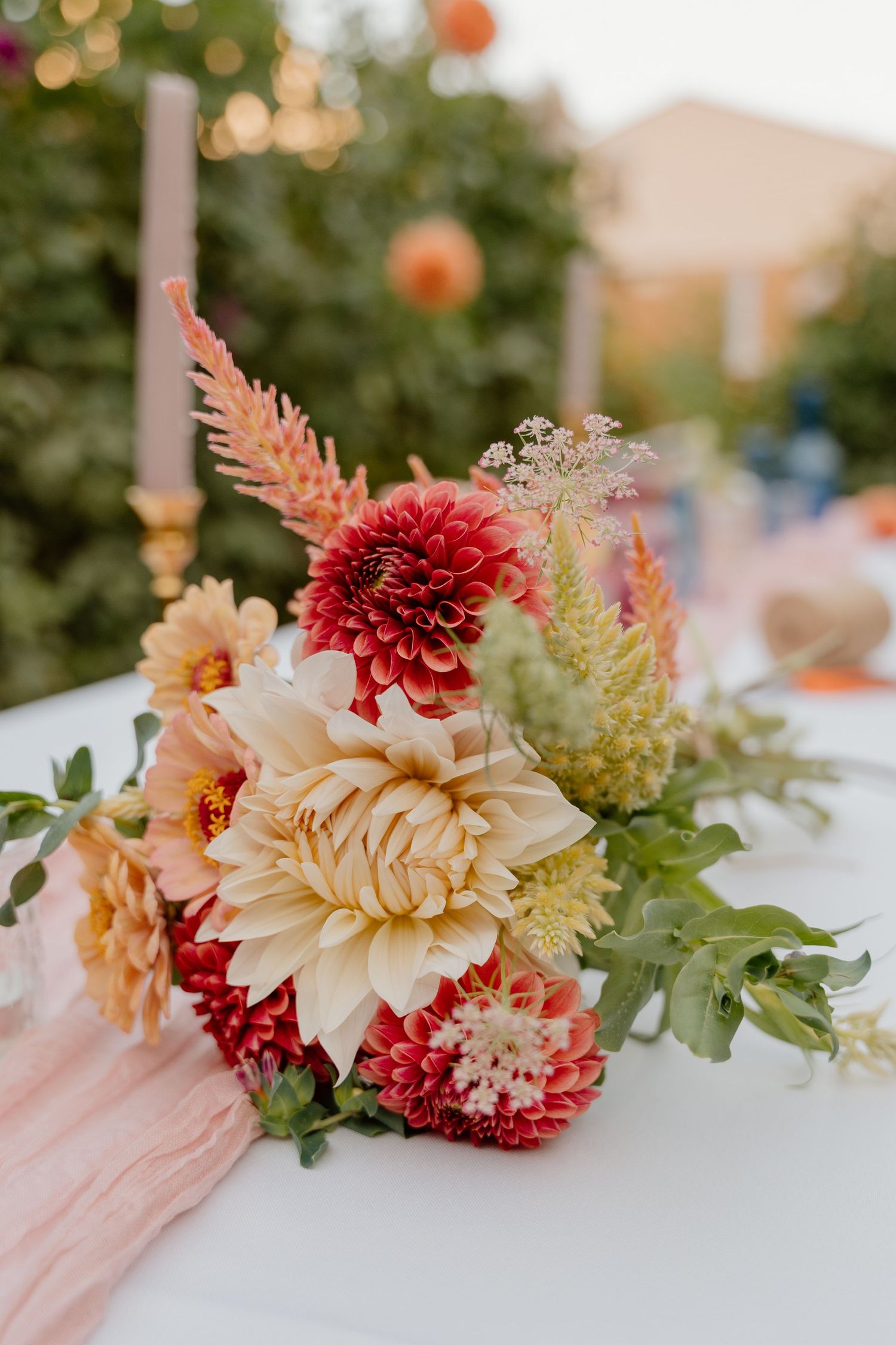 Elegant floral centerpiece featuring cream and burgundy dahlias with delicate greenery on a white tablecloth.