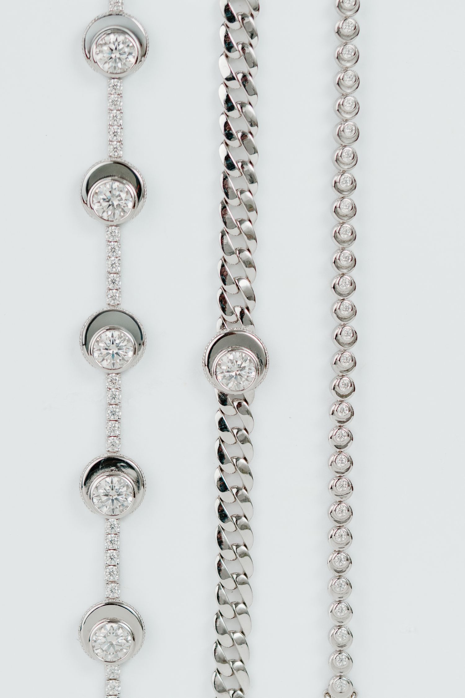 Elegant silver necklaces with diamond bezel settings arranged in a vertical display on white background.