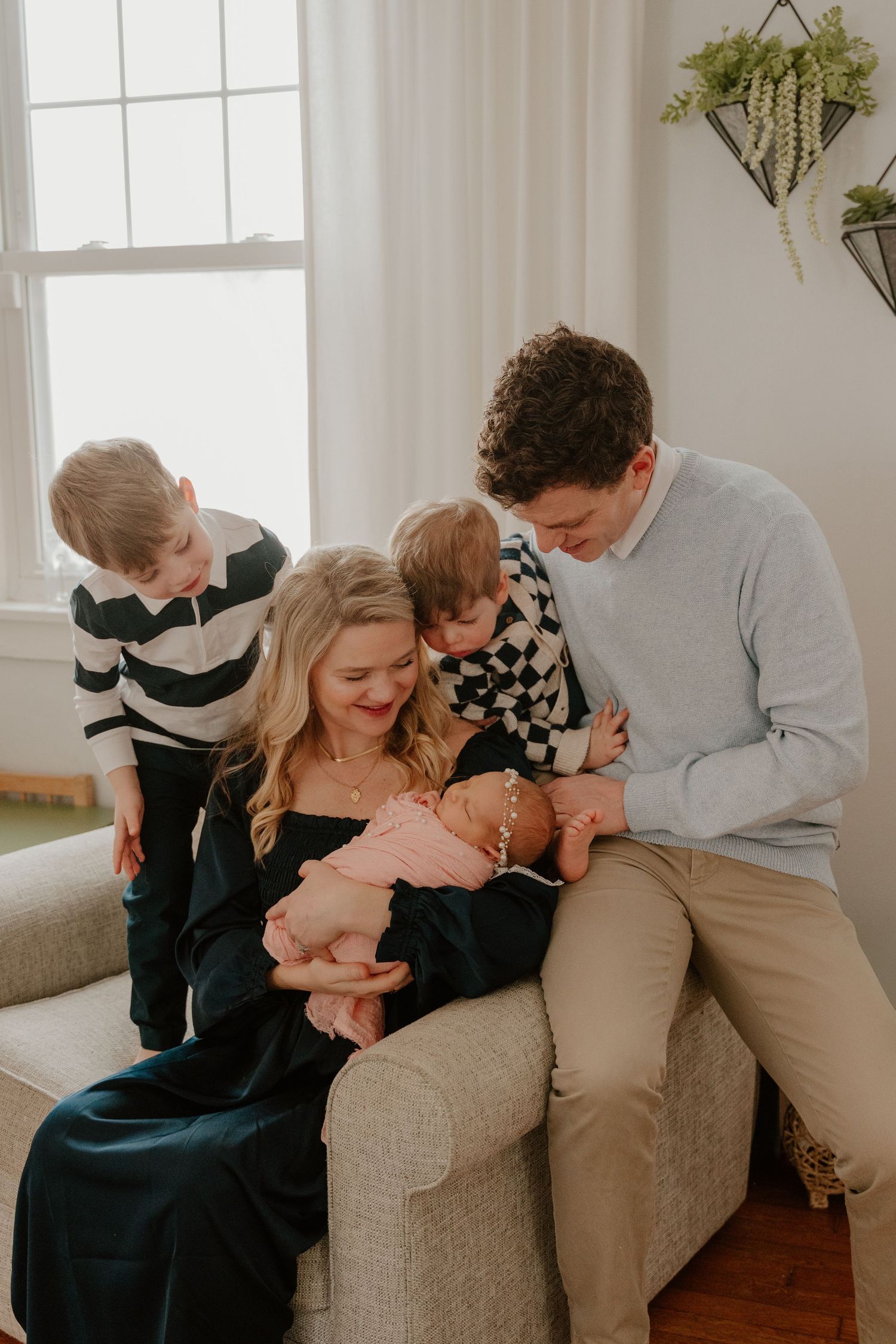 Family members share loving embraces while sitting together on a beige couch in a bright living room.