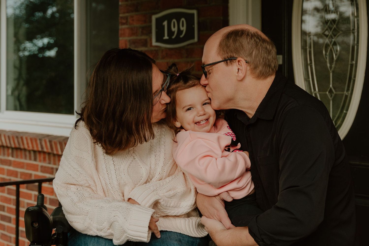 A family shares a tender moment together on their front porch, laughing and embracing near house number 199.