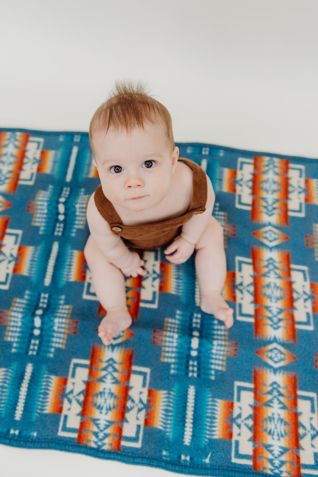Baby sitting on southwestern print blanket in turquoise and orange geometric patterns.