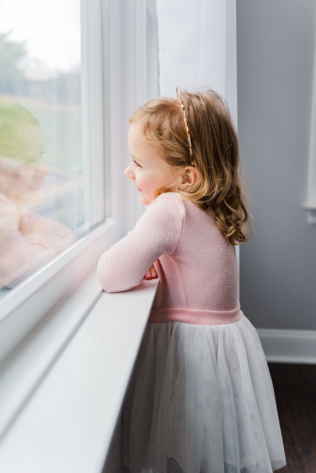 4 year old looks out window and smiles at reflection