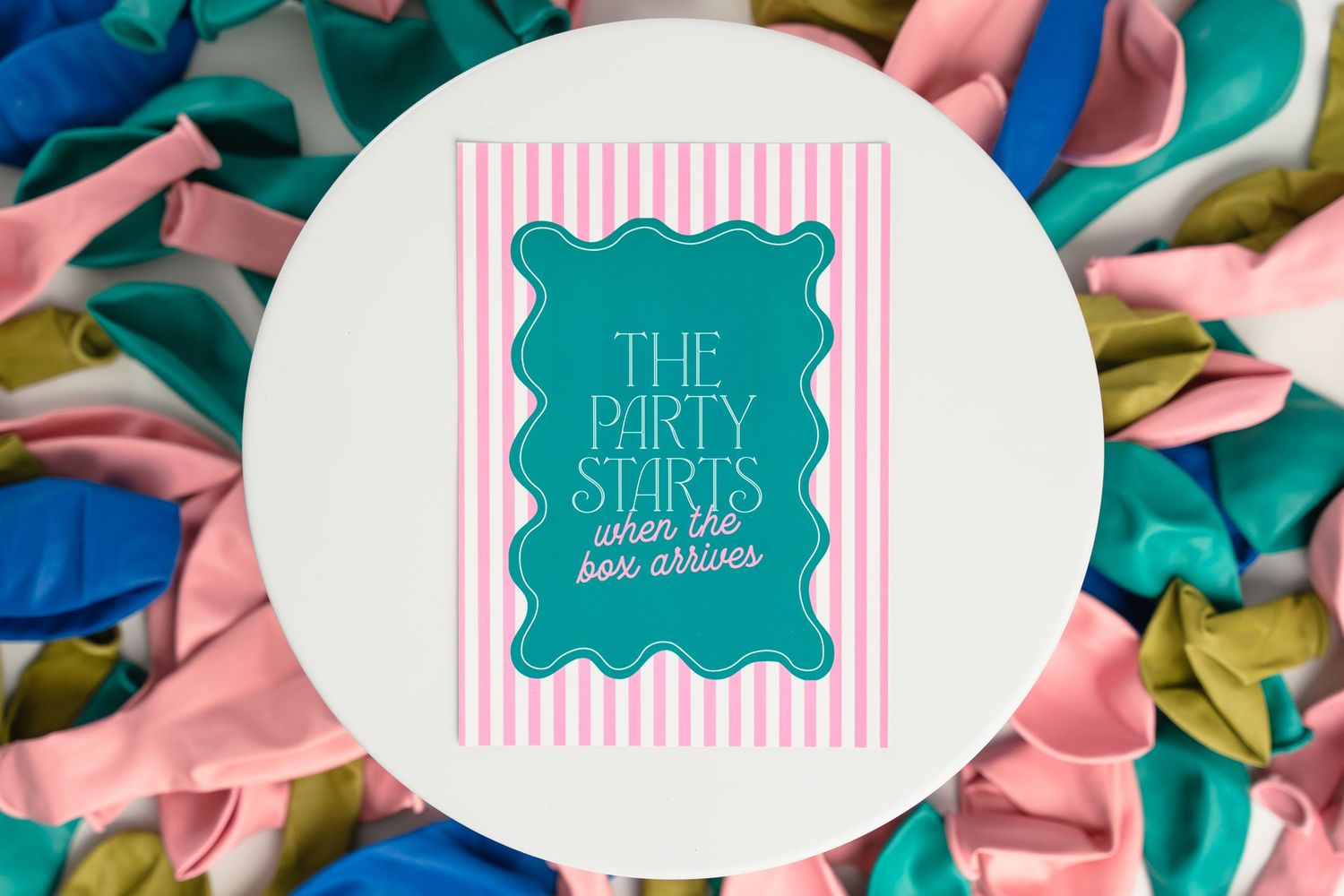 A teal and white party supplies logo on a round coaster surrounded by colorful tissue paper decorations.