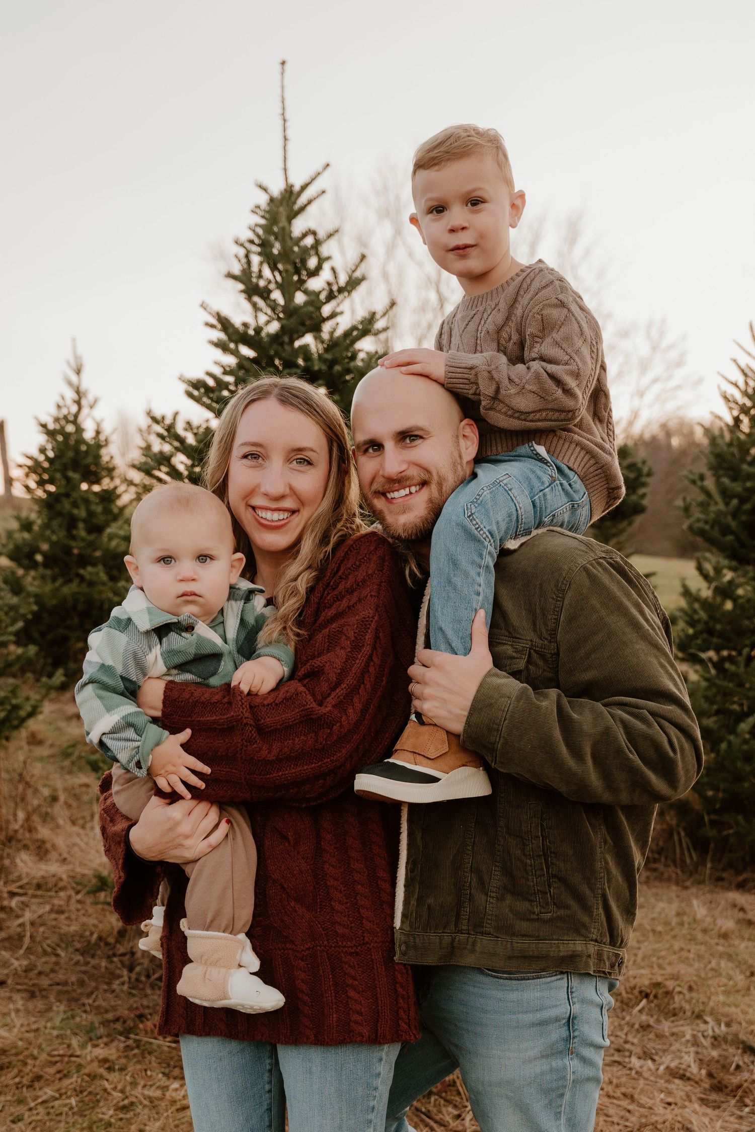 Family poses together in front of evergreen trees during an autumn outdoor photo session at sunset.