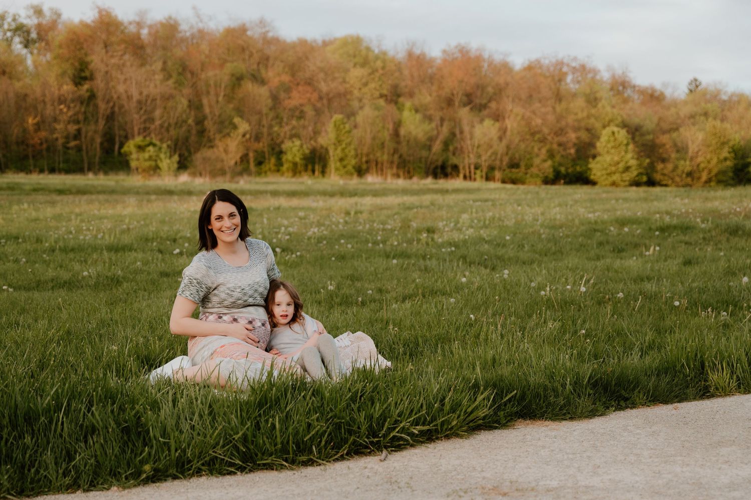 Mother and child sitting together on blanket in spring meadow near path.