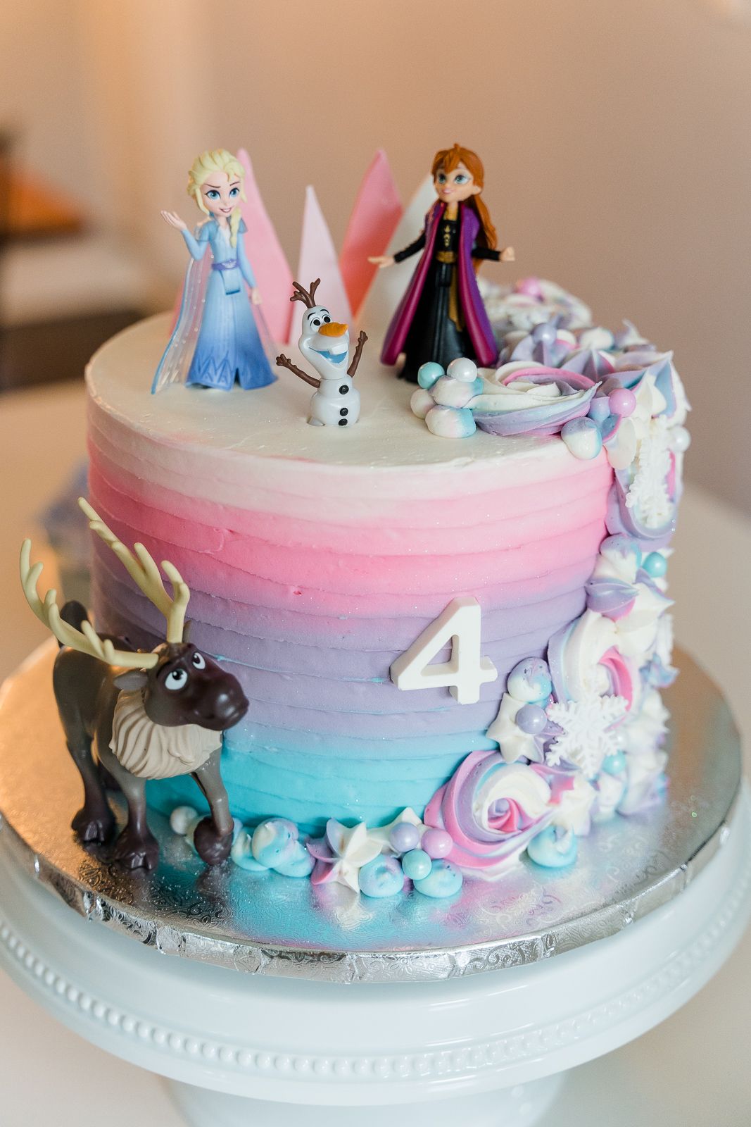 Frozen themed birthday cake with Elsa, Anna and Olaf figurines on pink and blue ombre frosting.