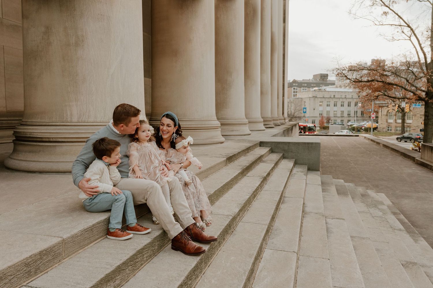 A family sits together on grand stone steps of a classical building during a photo session.
