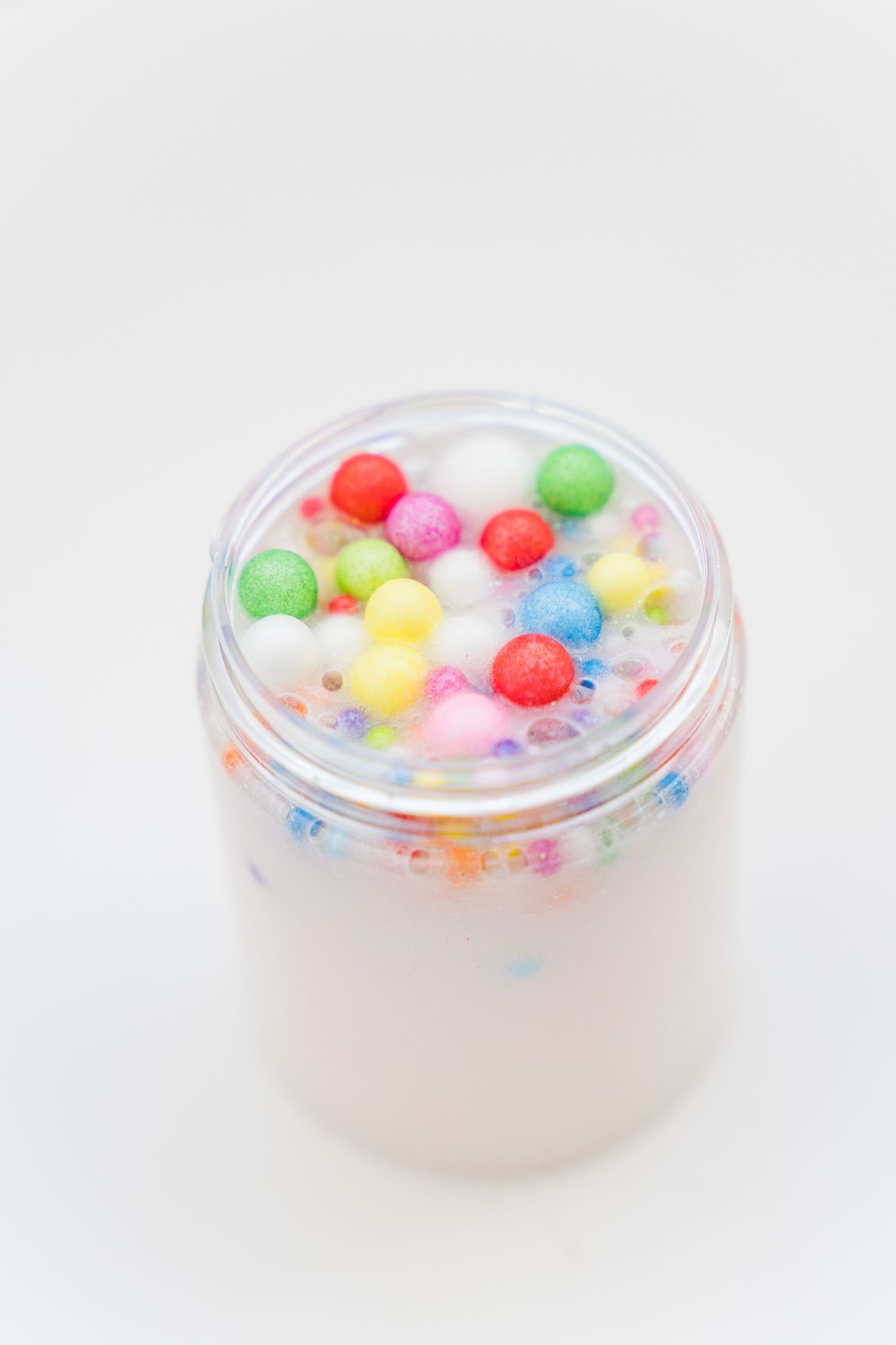 Colorful foam pom poms and glitter stars float in clear slime inside a transparent container.