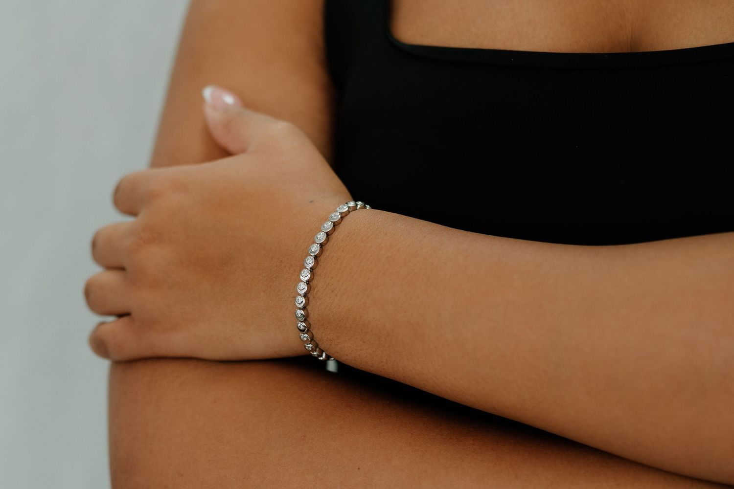Close-up view of hands wearing delicate silver and diamond tennis bracelets against a dark background.