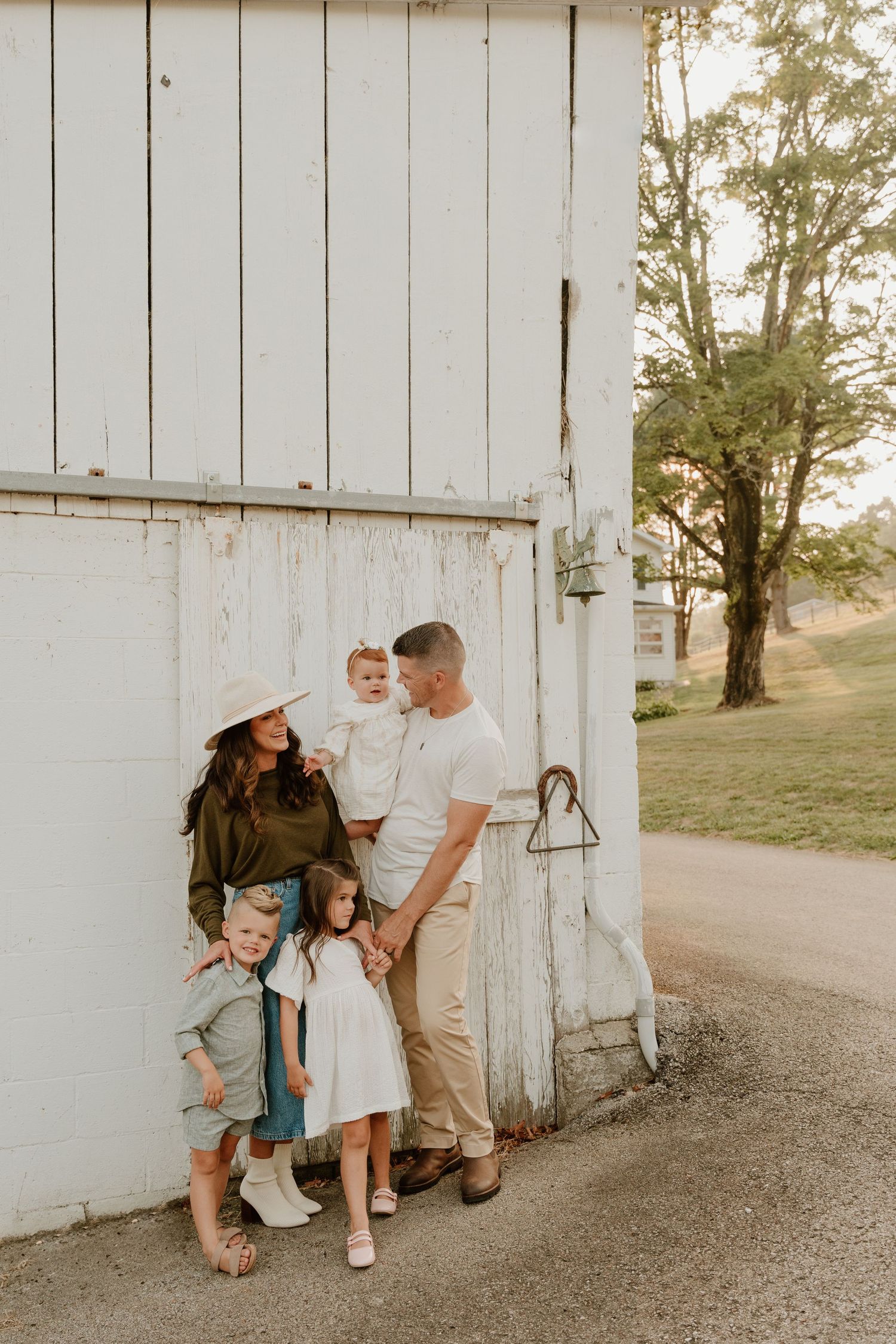 A family shares tender moments against a rustic white barn wall in warm golden light.