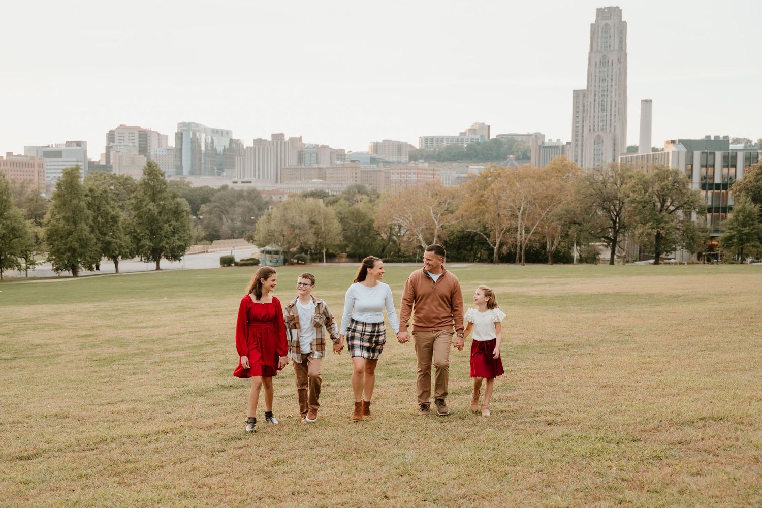 A group of people walk together across a grassy field on an autumn day with trees in the background.