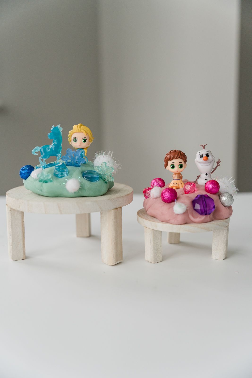 Small Frozen-themed decorative displays featuring Elsa and Anna figurines with colorful ornaments on wooden stands.