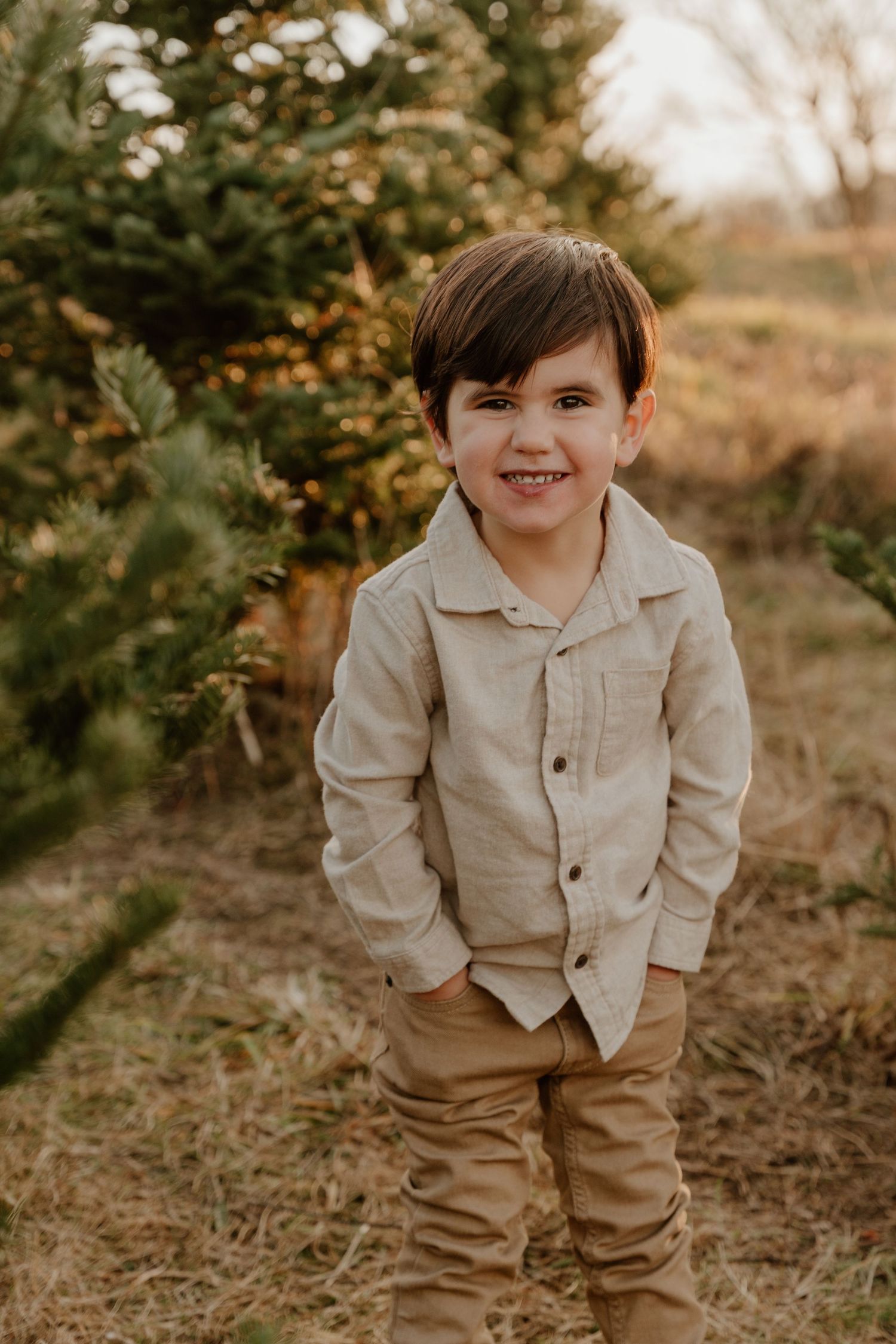 A young child in beige clothing poses playfully outdoors in a natural autumn setting.