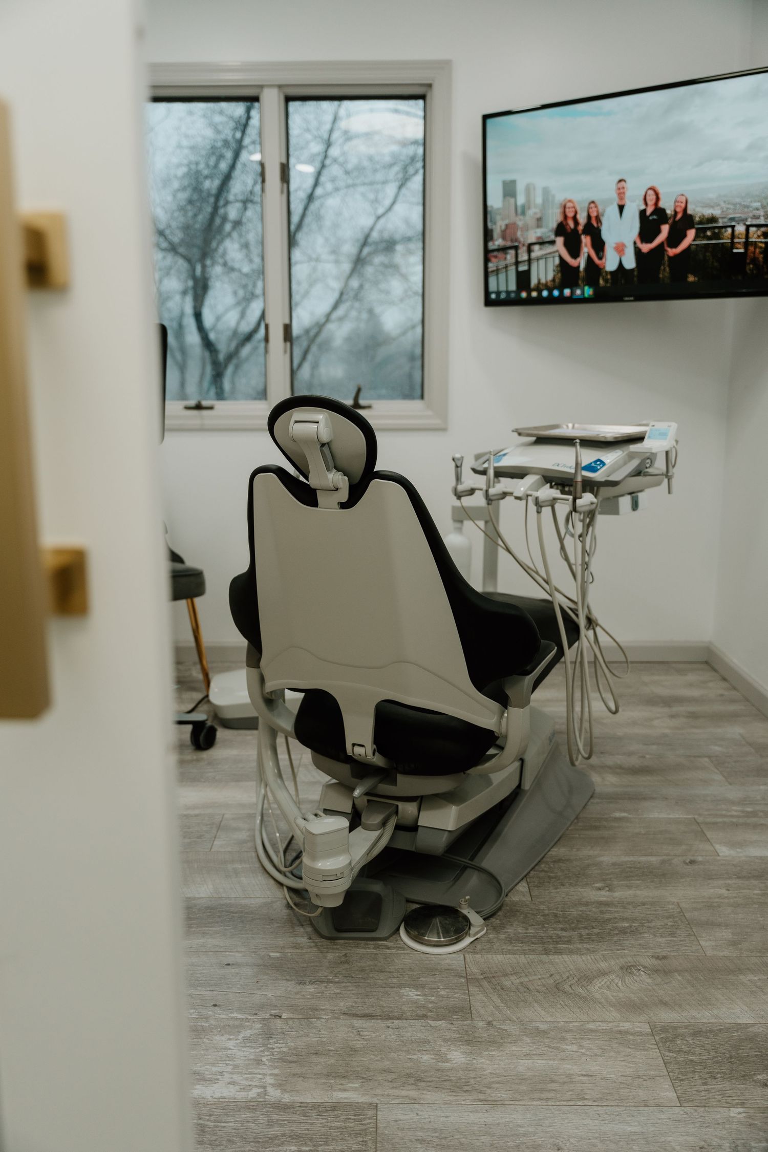 Modern dental office interior with five treatment chairs arranged in a bright space with large windows and hardwood flooring.