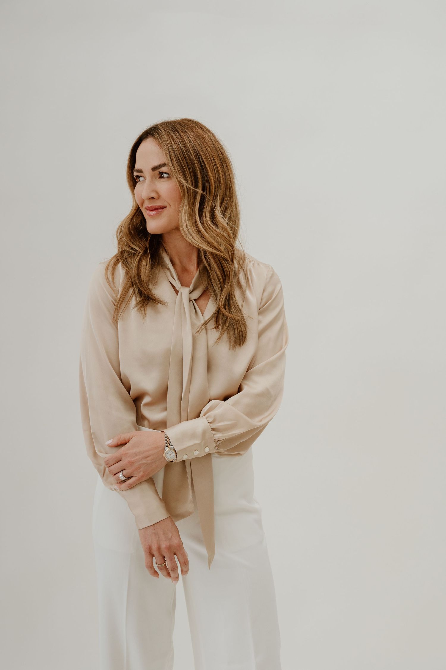 A person wearing a beige button-up shirt poses against a white background in a minimalist fashion photoshoot series.