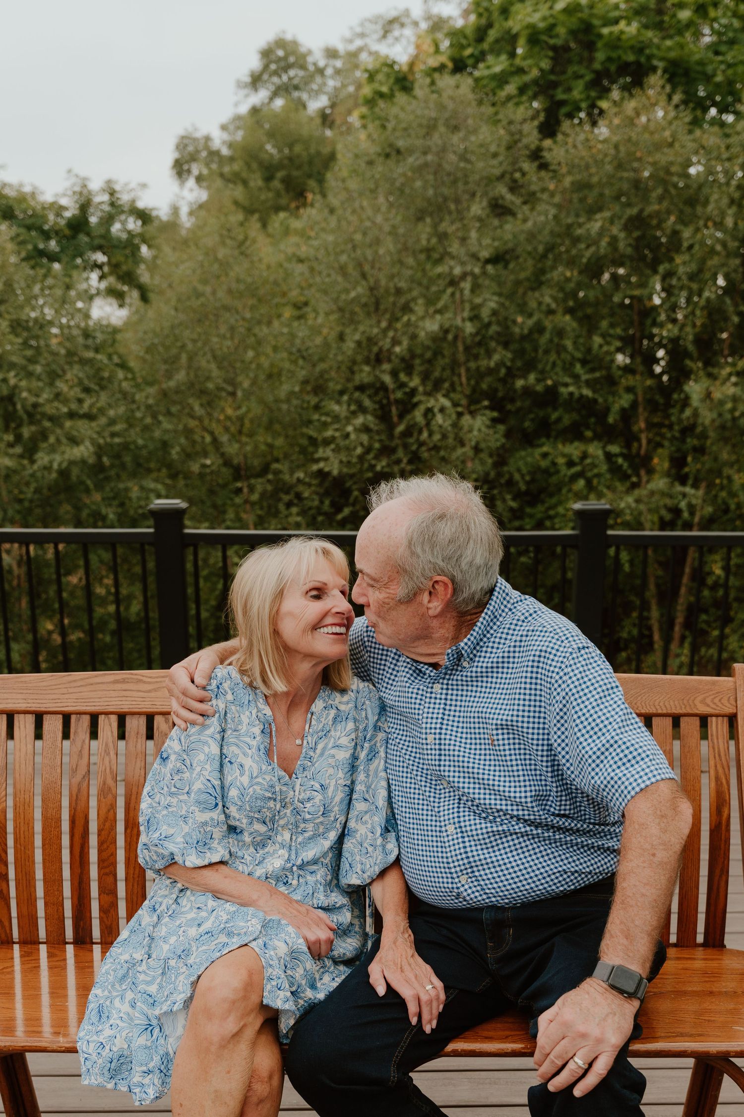 Senior couple sharing tender moments while sitting together on a wooden park bench in a natural outdoor setting.