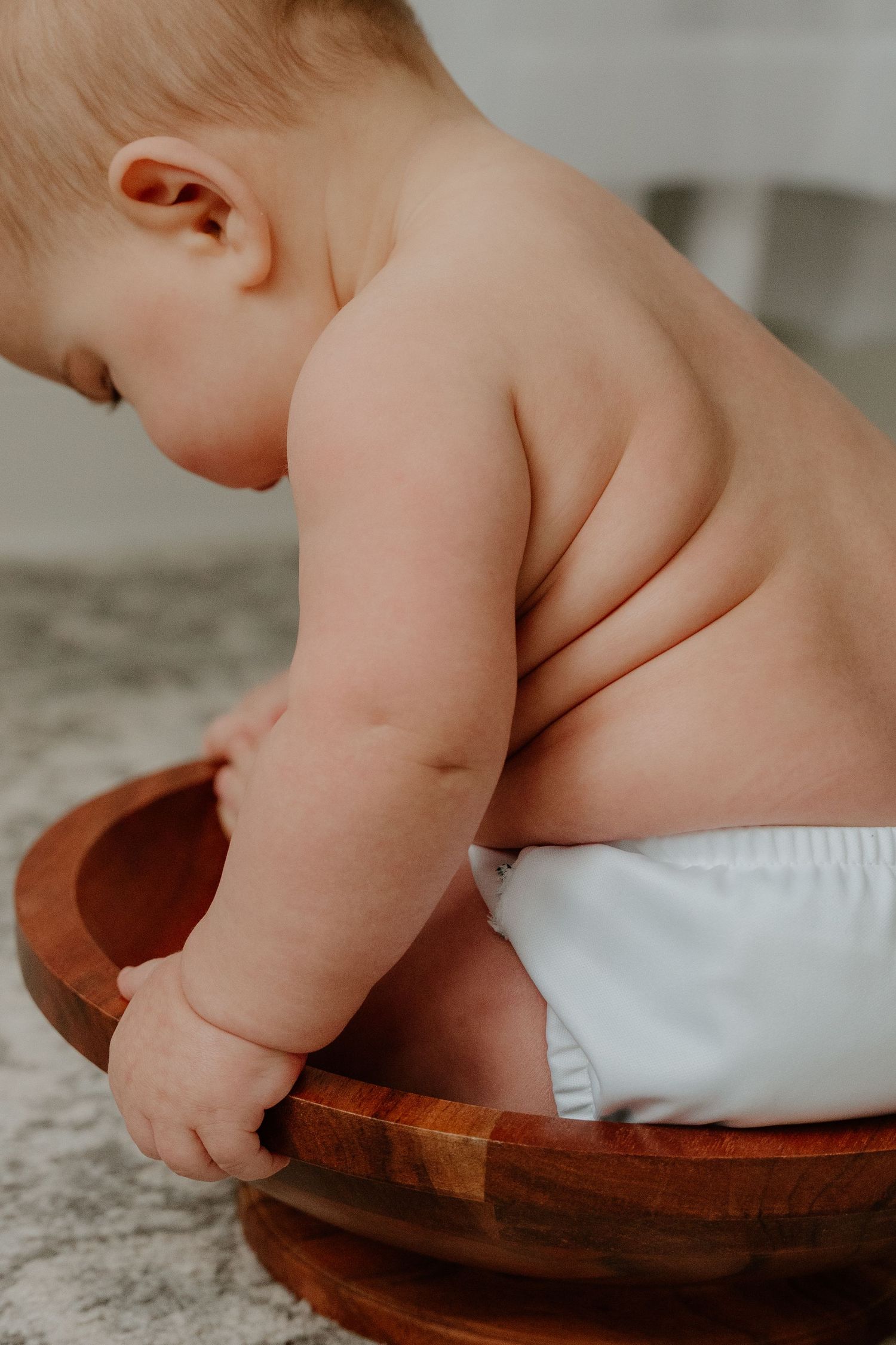 Close-up view of a baby's chubby legs and feet resting on a wooden surface with white fabric.