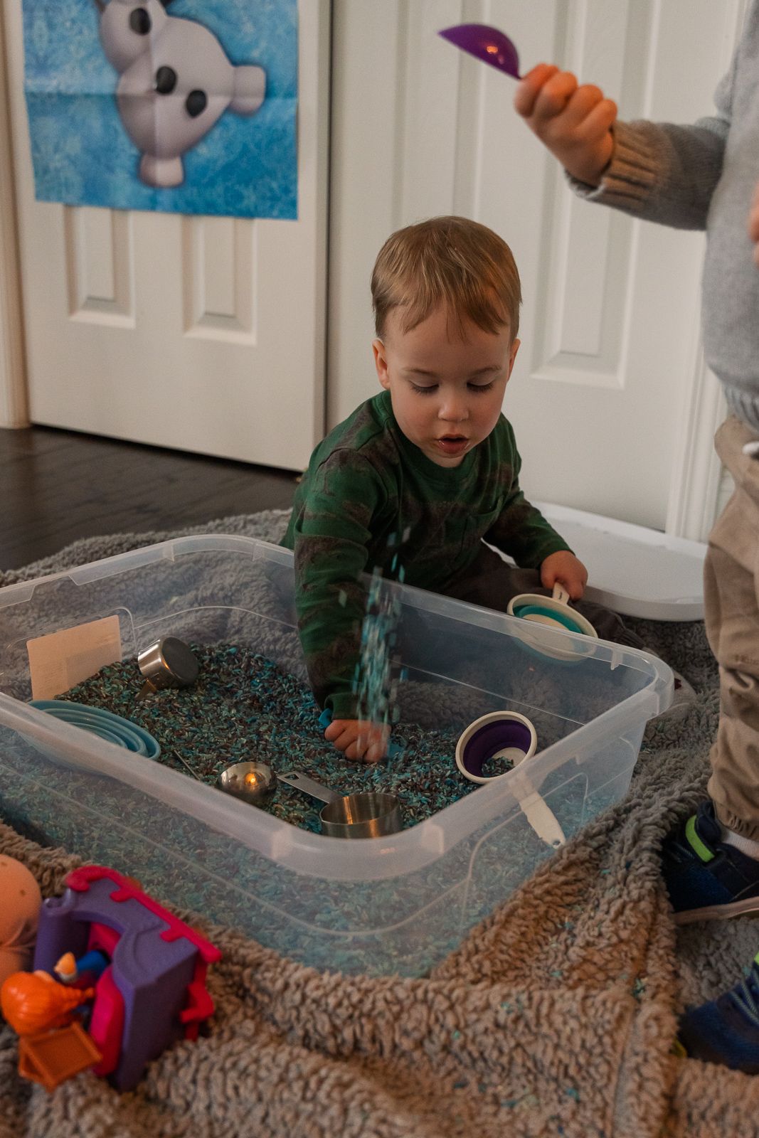 Interactive sensory bin play setup with blue rice and activity tools on carpet.