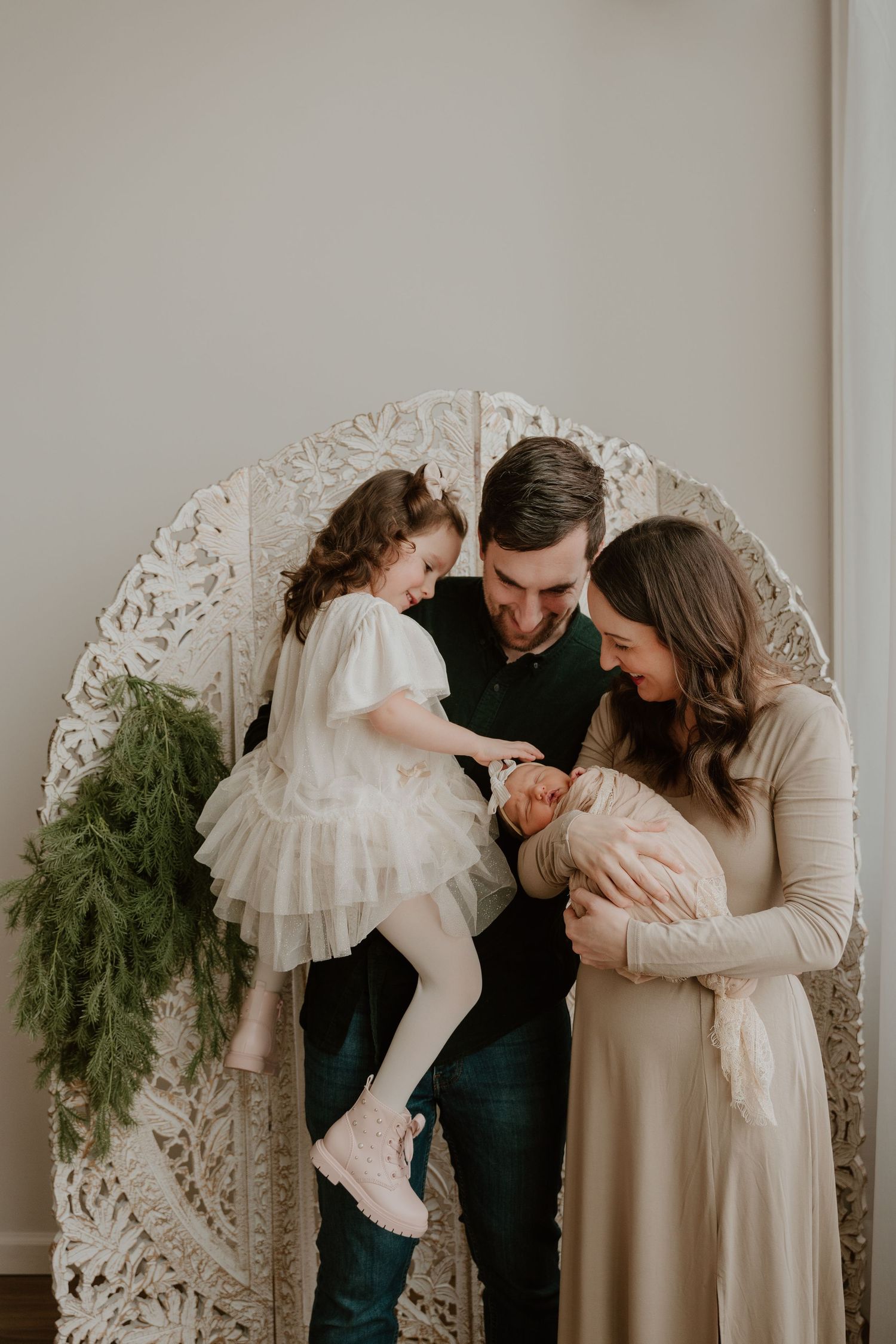 Family poses together in front of decorative white arch with greenery for an intimate indoor portrait session.