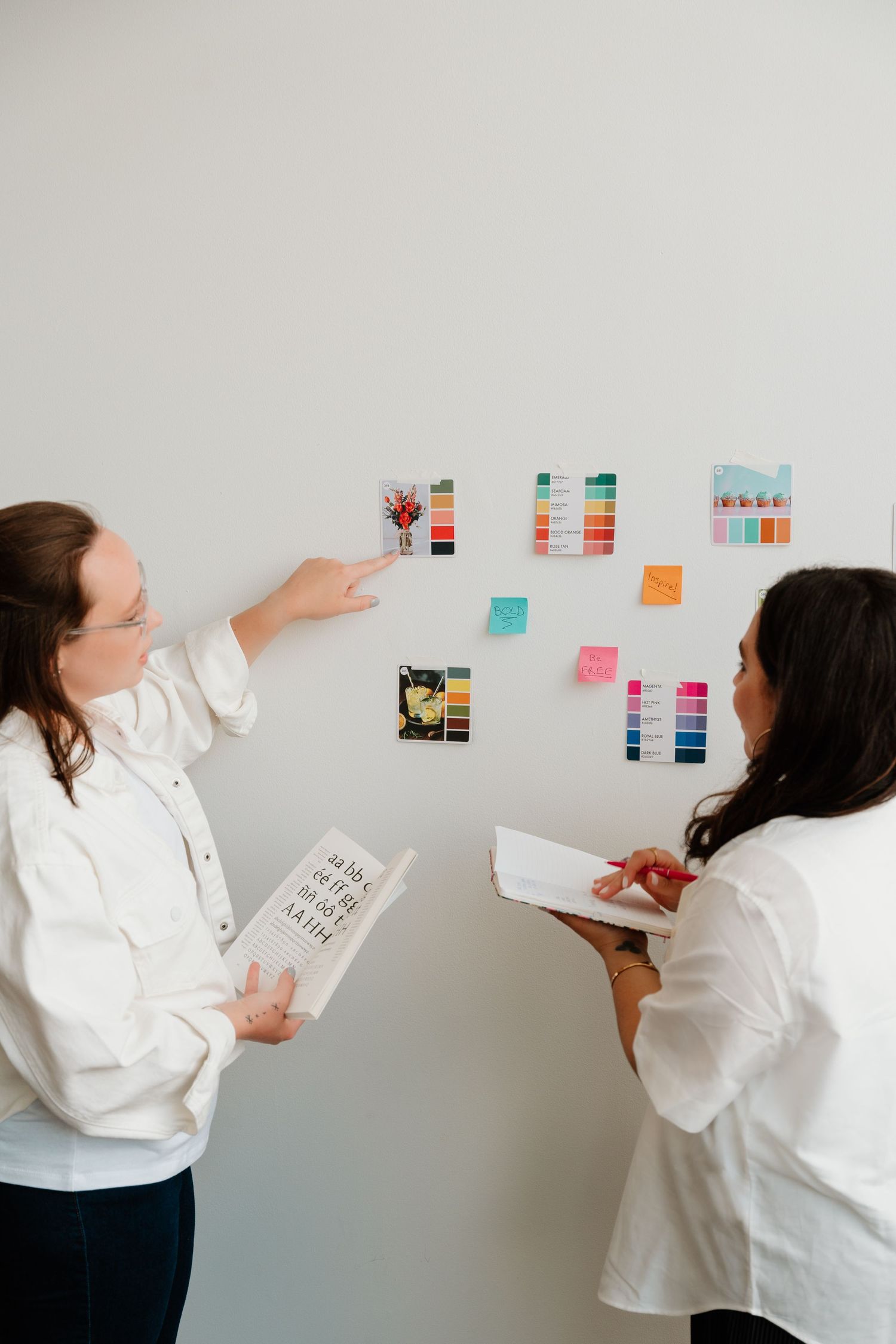 Two people in white shirts collaboratively arranging colorful sticky notes and papers on a white wall during a planning session.