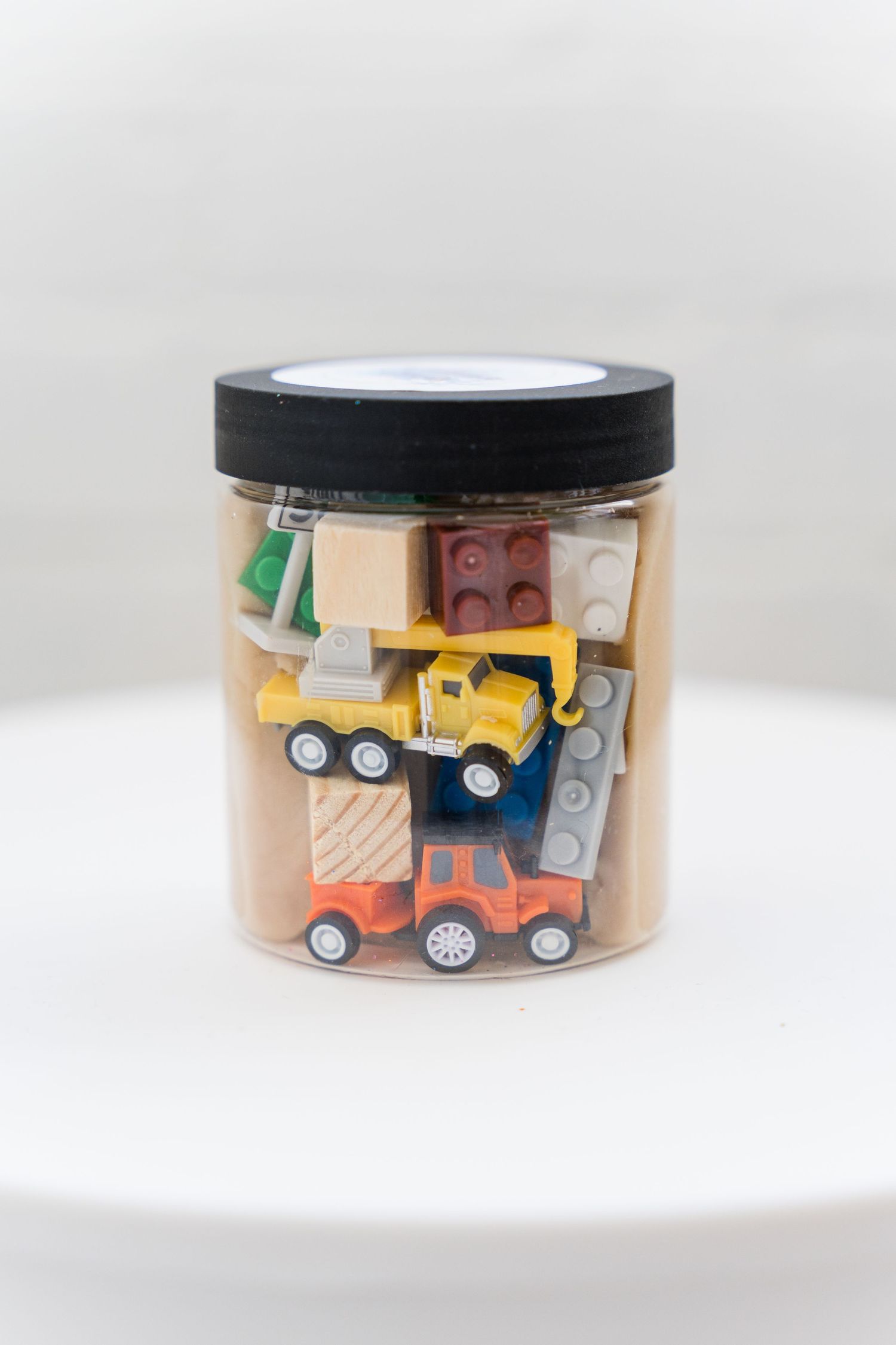 Clear storage jar filled with colorful toy cars and trucks with black lid displayed from different angles.