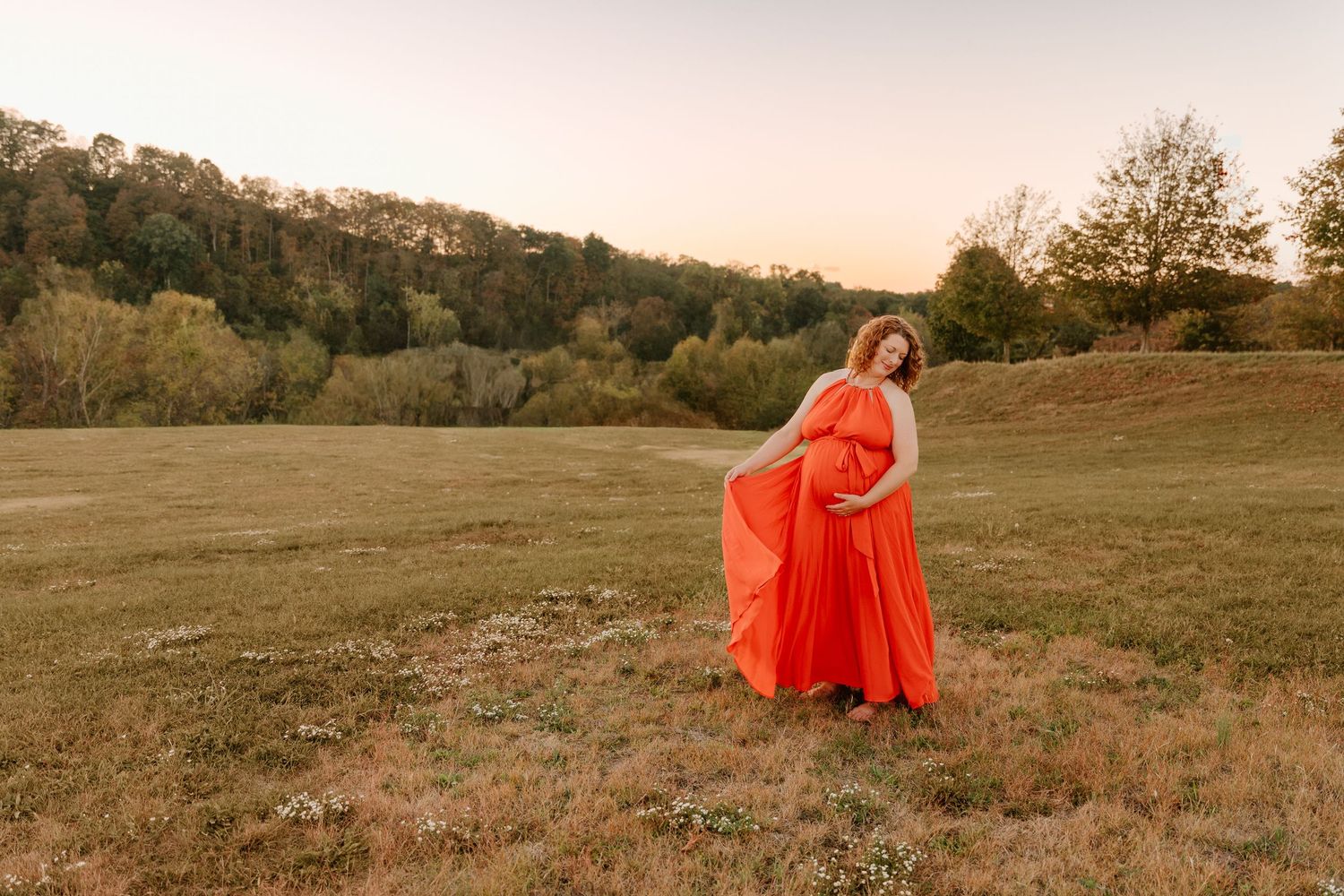 A figure in a flowing orange dress stands in a golden field during sunset, creating a dreamy ethereal scene.