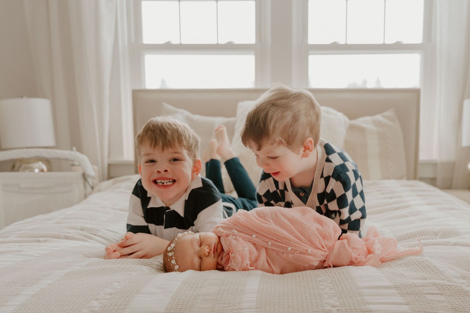 Children lie on white bedding in a row, creating a playful and candid lifestyle scene.