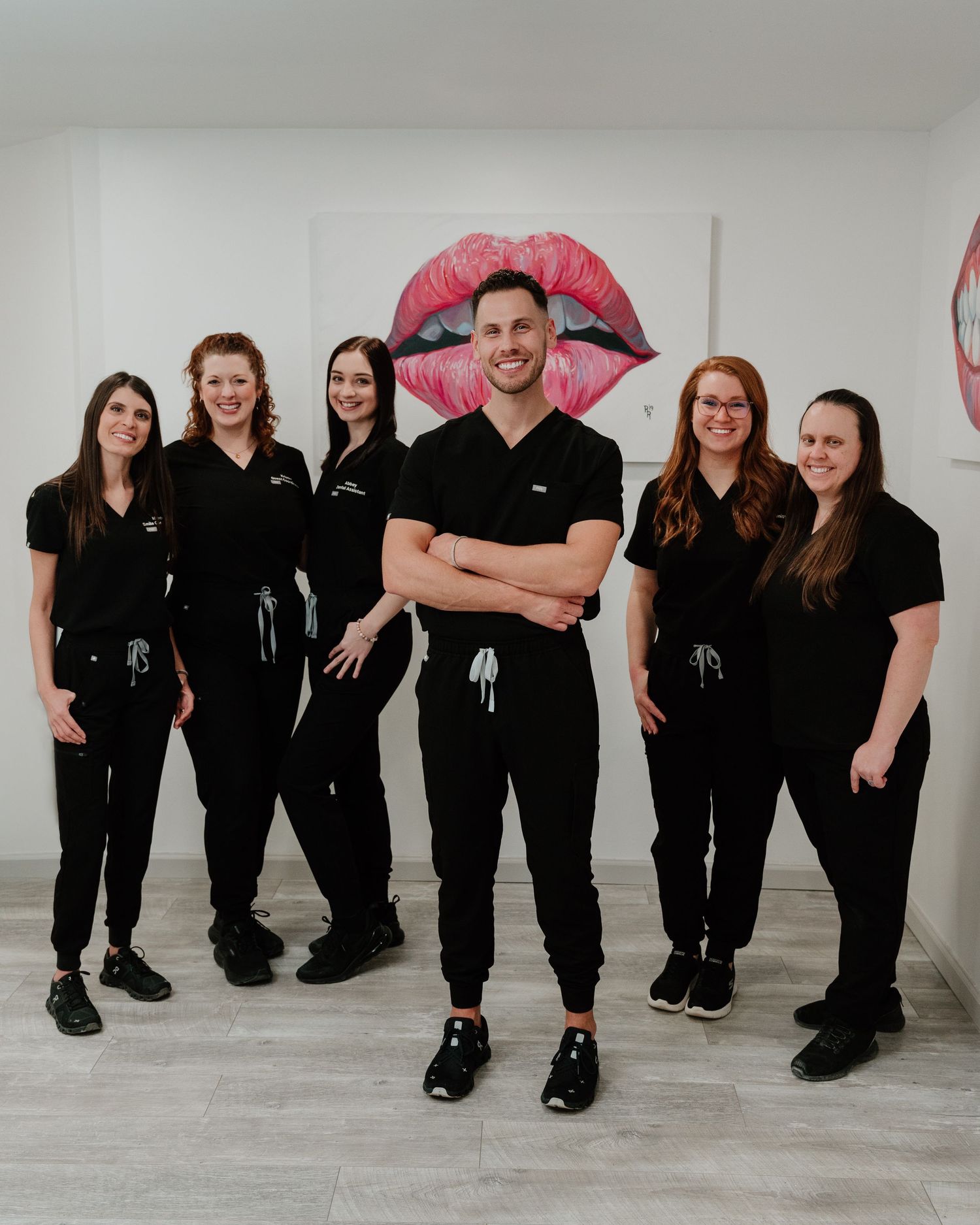 Group photo of people in black outfits posing against white wall with red lip artwork decorations.
