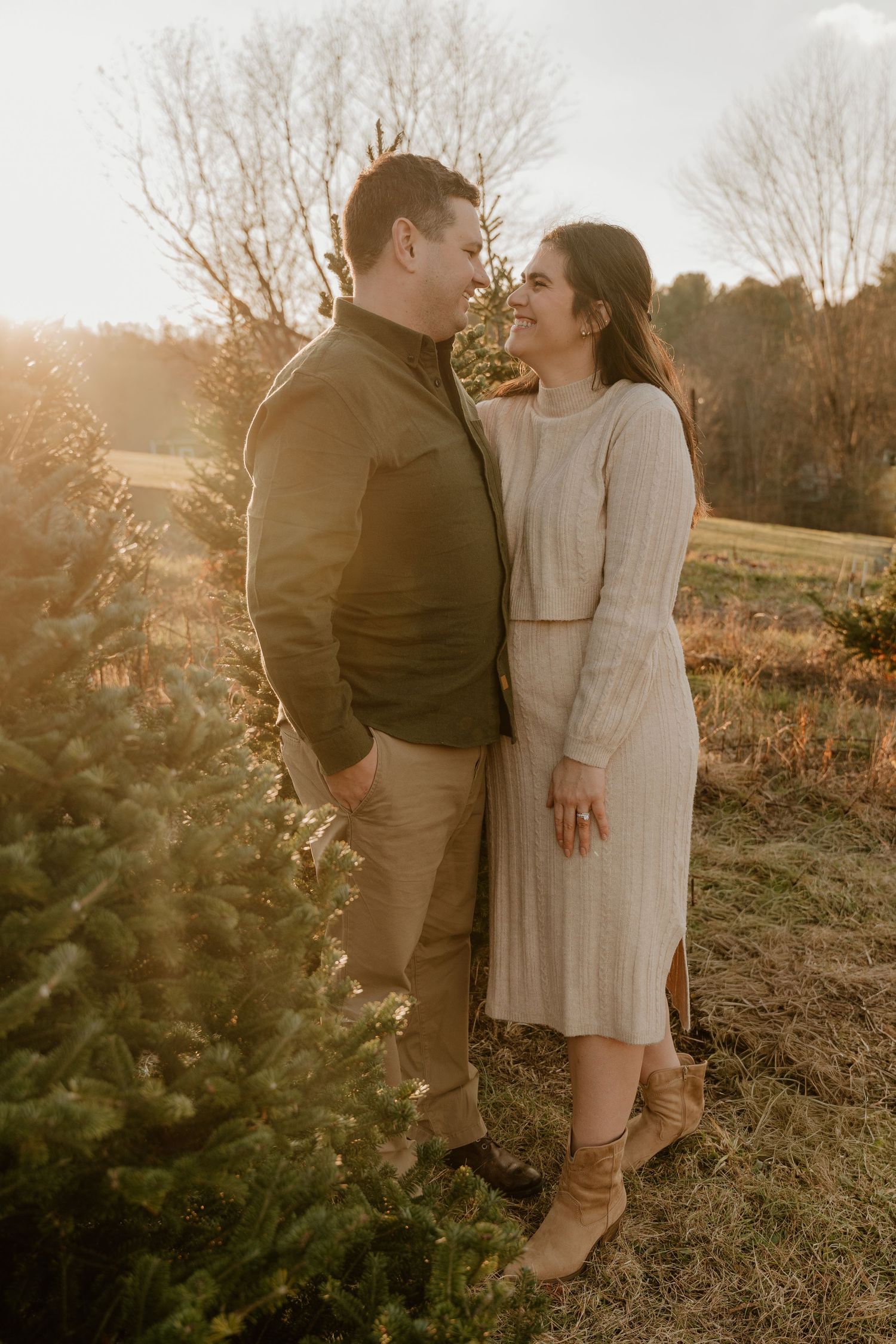 A couple embraces in a romantic outdoor photoshoot during golden hour with bare trees and natural scenery in the background.