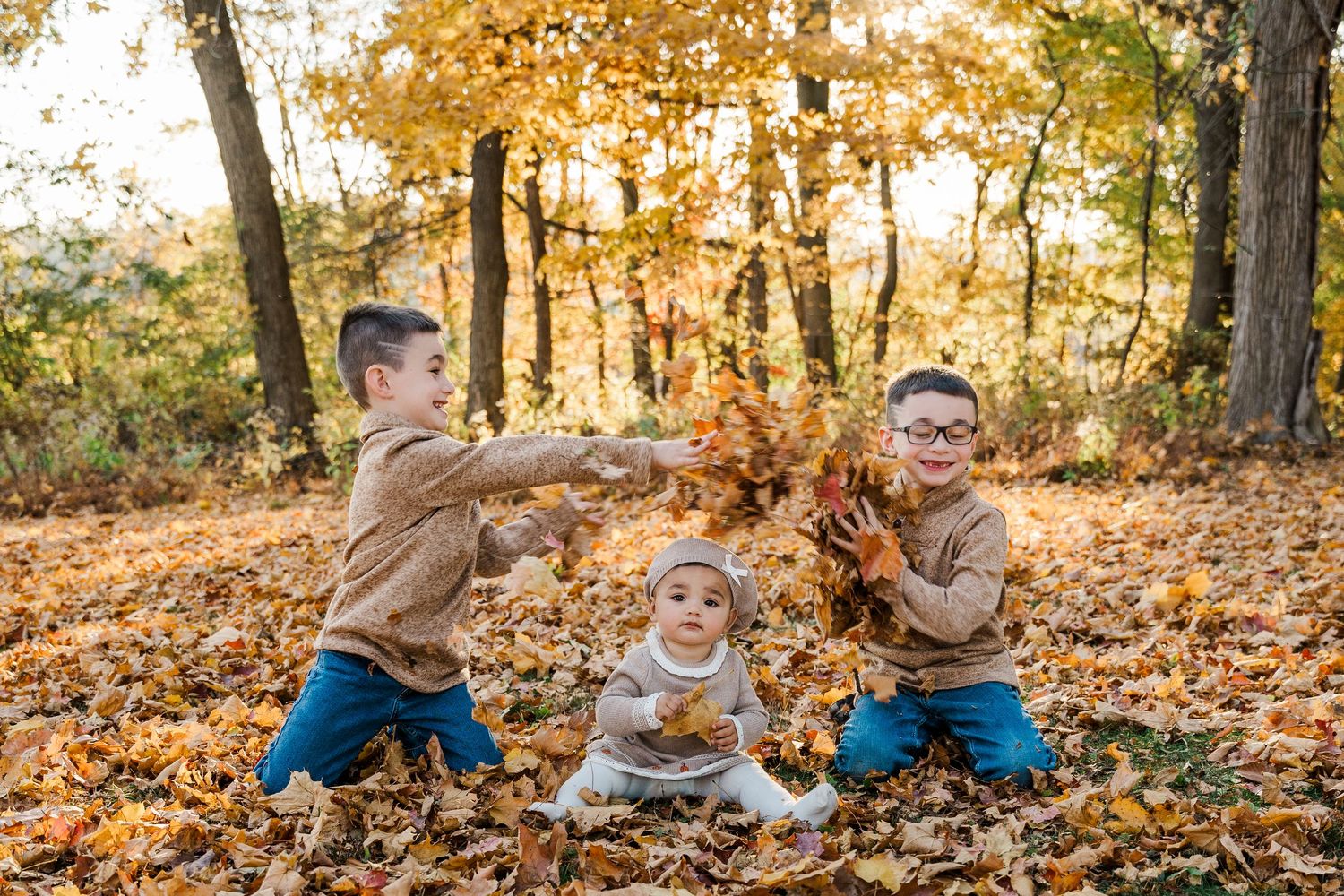 Children playing and throwing fall leaves in autumn forest setting.