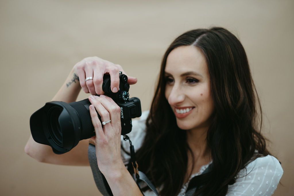 Portrait of photographer holding professional camera against neutral background.