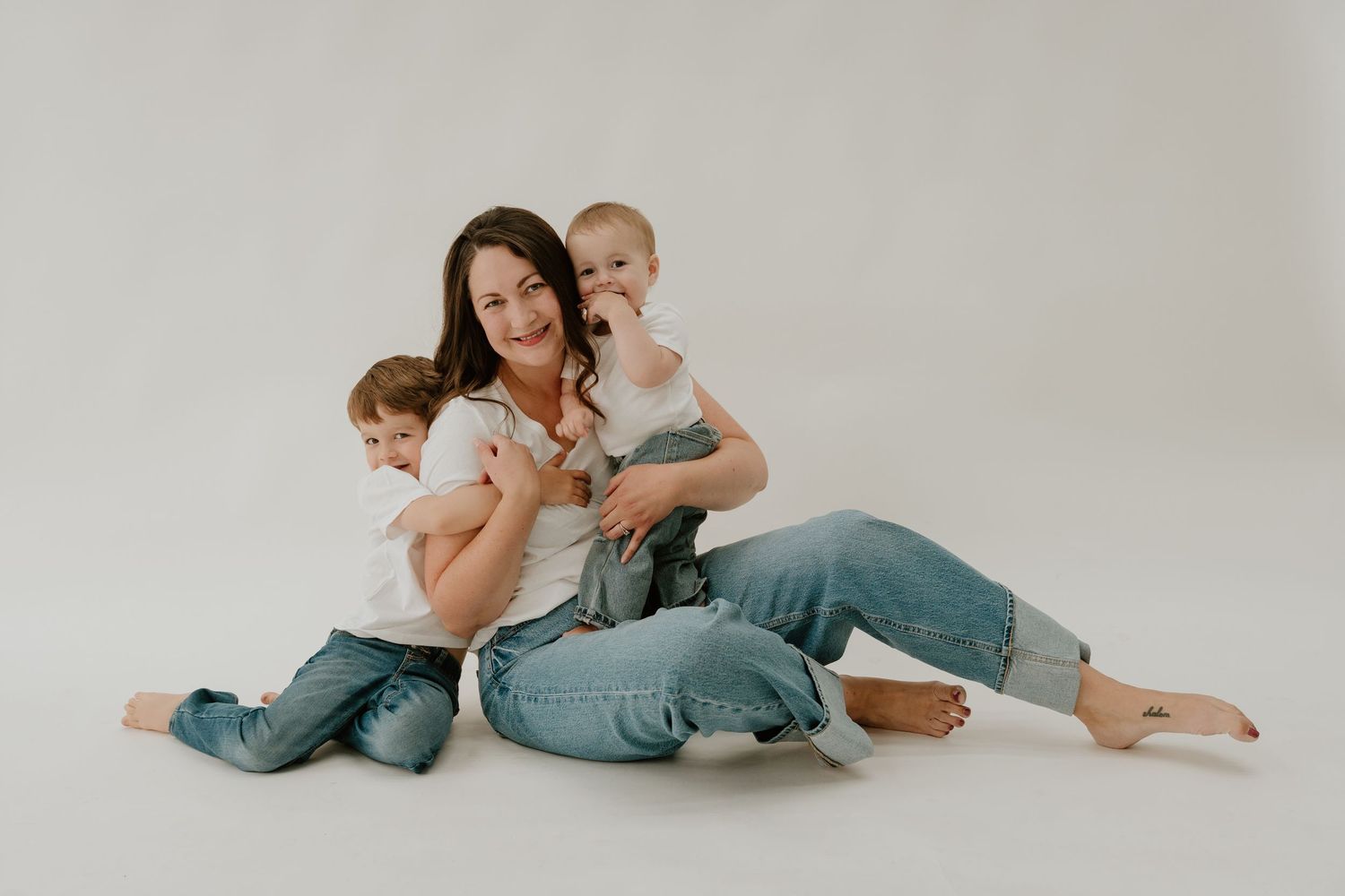 Family lounging together on white floor in coordinated casual outfits during indoor photoshoot.