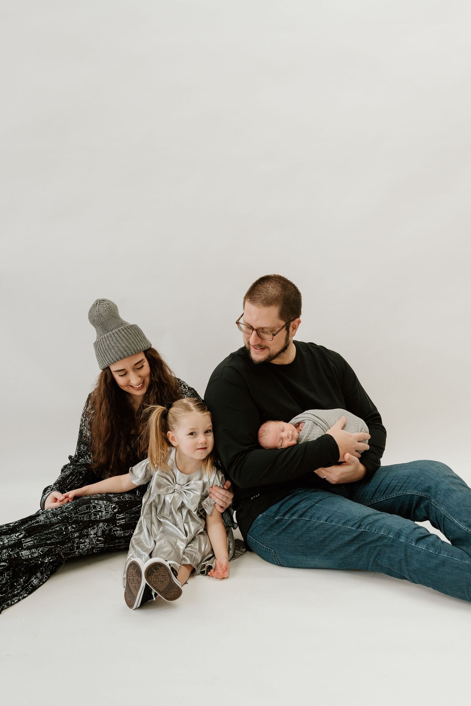 Family with young children sitting together on white floor during indoor studio photography session.